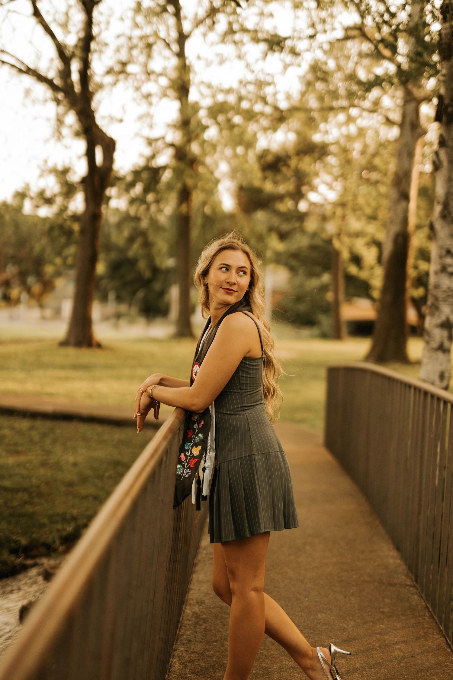 Someone in a pleated dress poses along a railing in a park during sunset.