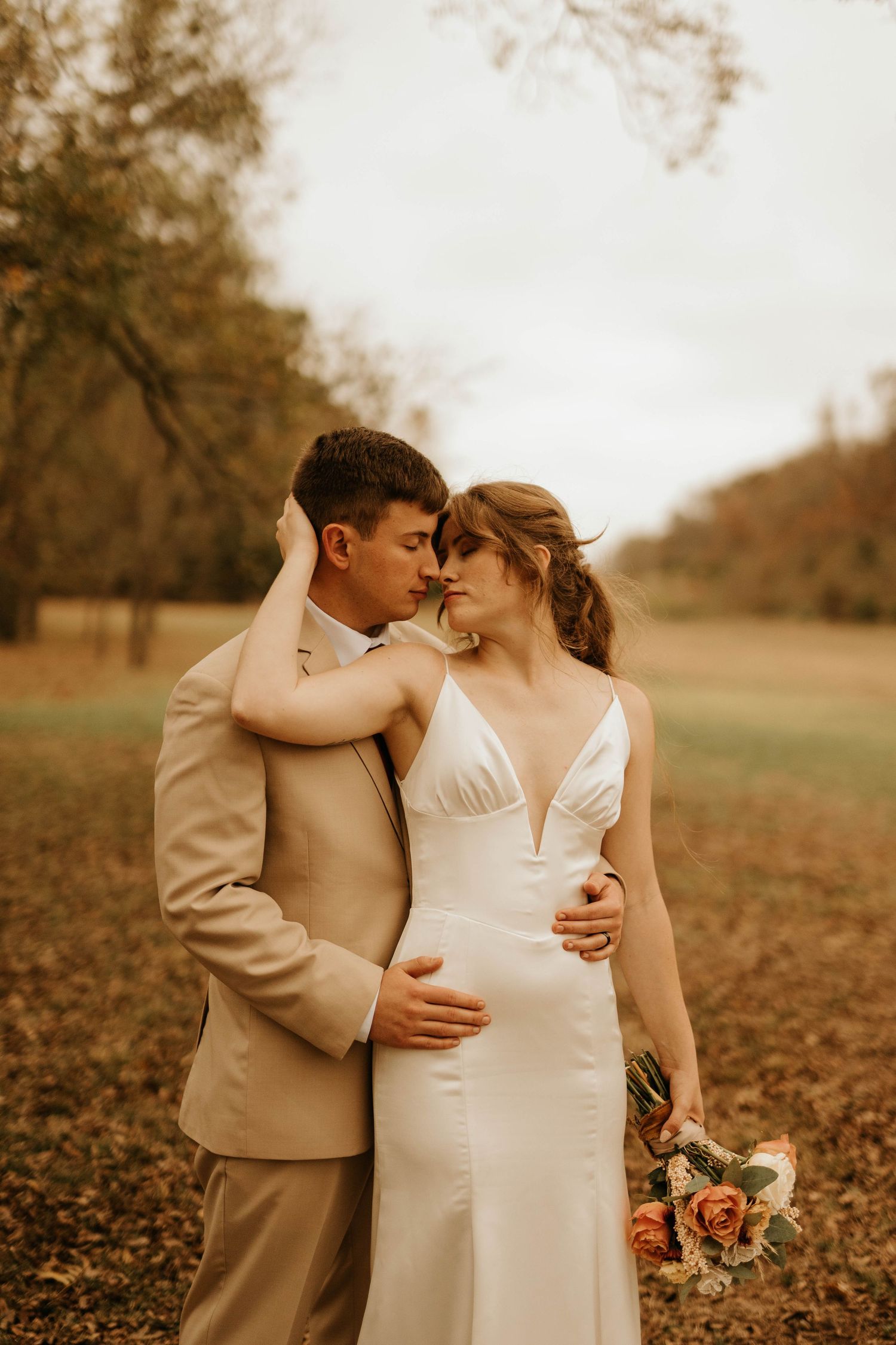 Intimate moment between bride and groom in tan suit embracing during golden hour portrait session.