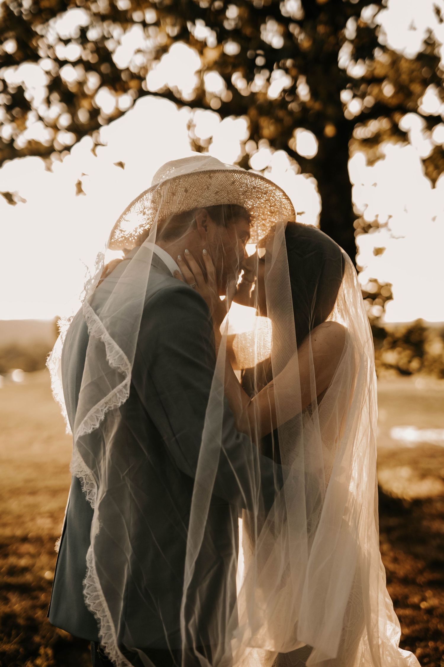 Silhouette of couple sharing intimate moment under veil during sunset wedding portraits.