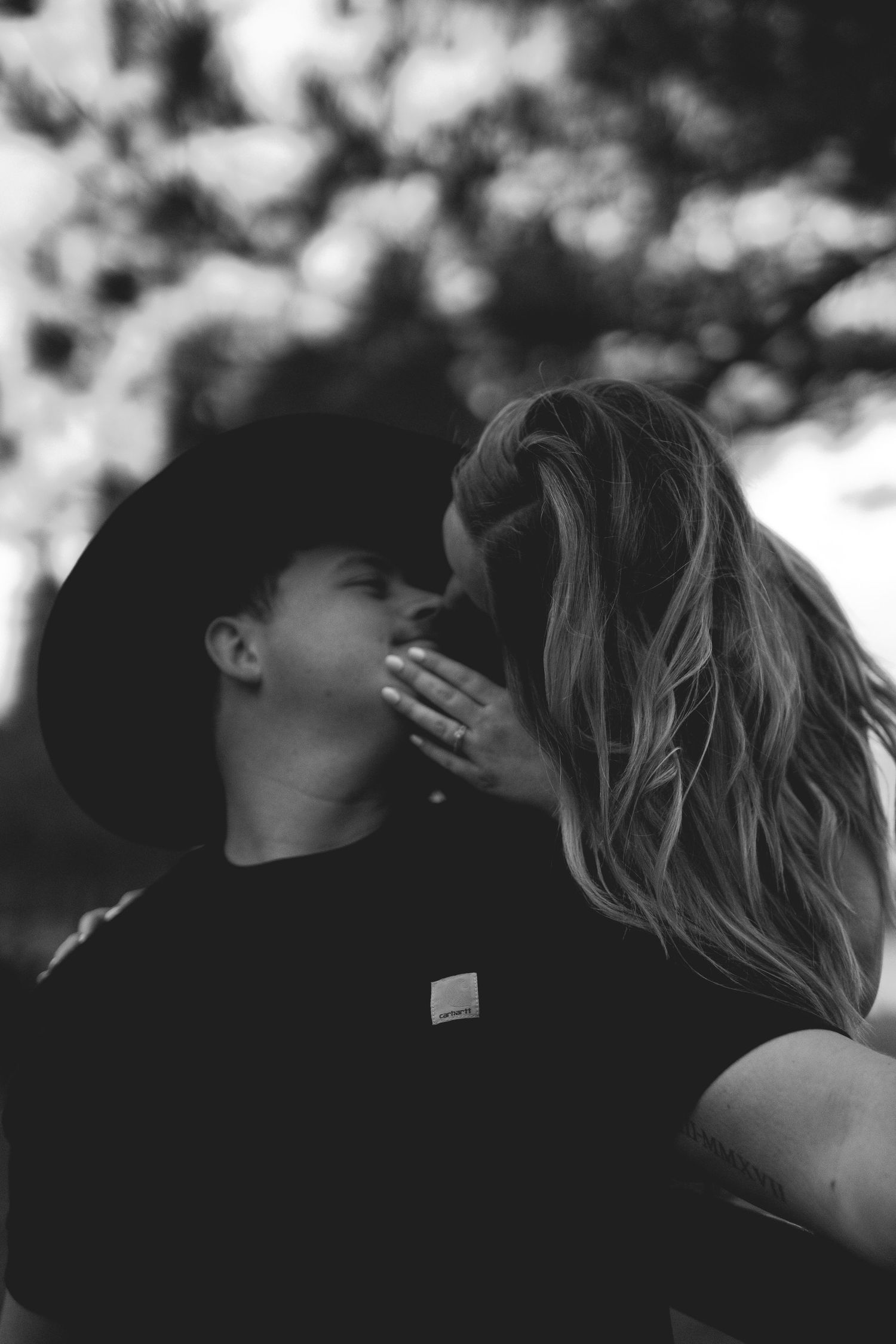 Black and white photo of a woman kissing a young boy wearing a cowboy hat outdoors.