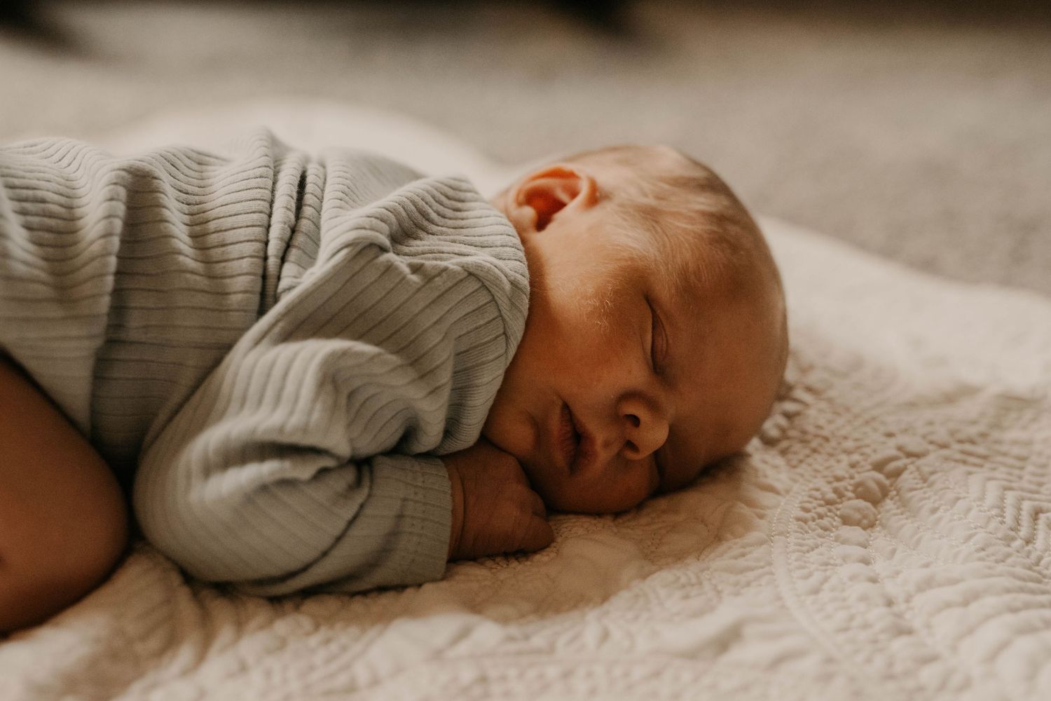 An infant rests peacefully on a soft cream-colored blanket.