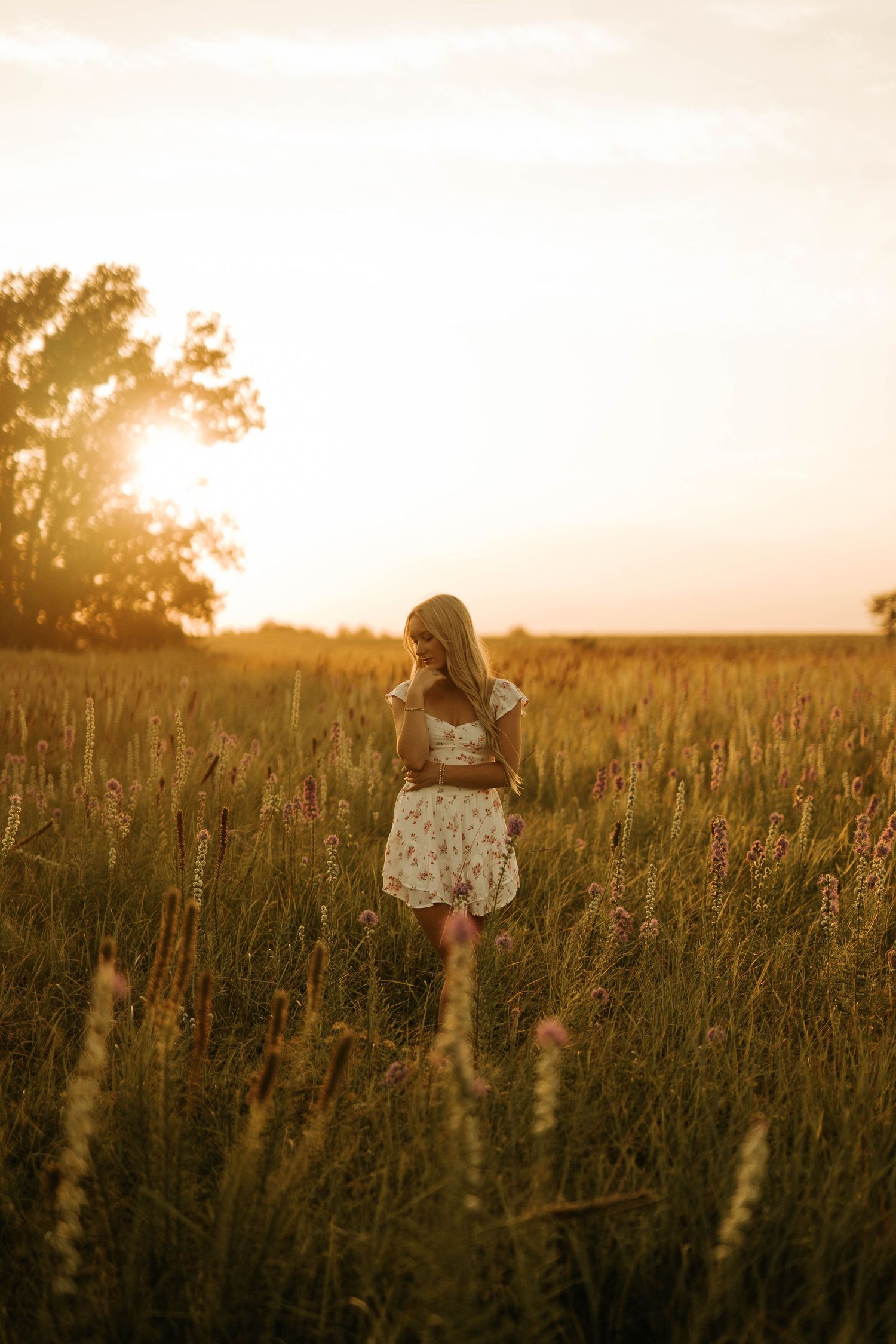 Young woman in floral dress standing in golden field at sunset.