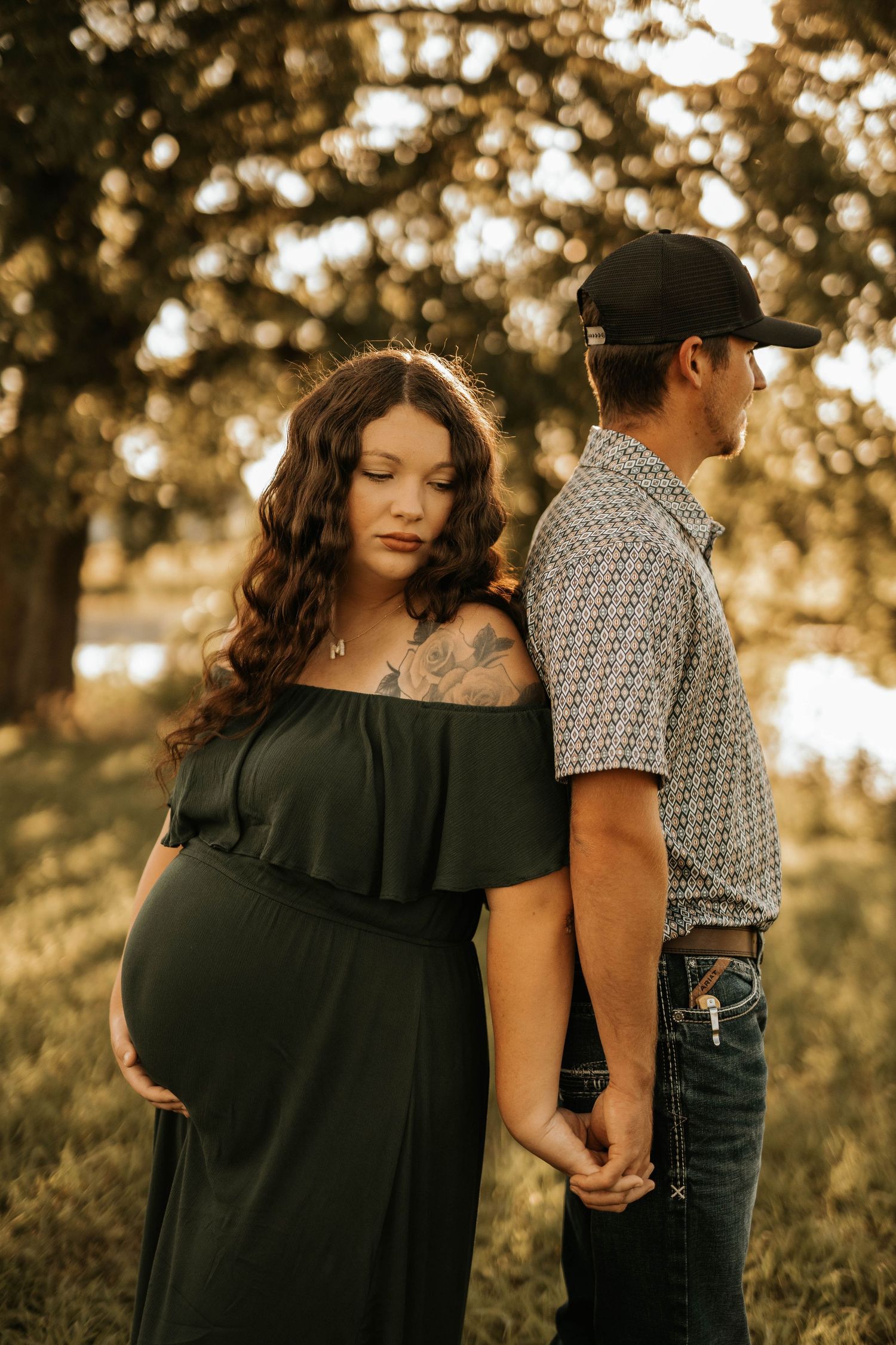 Expecting couple poses for maternity photo in a sunlit field at golden hour.