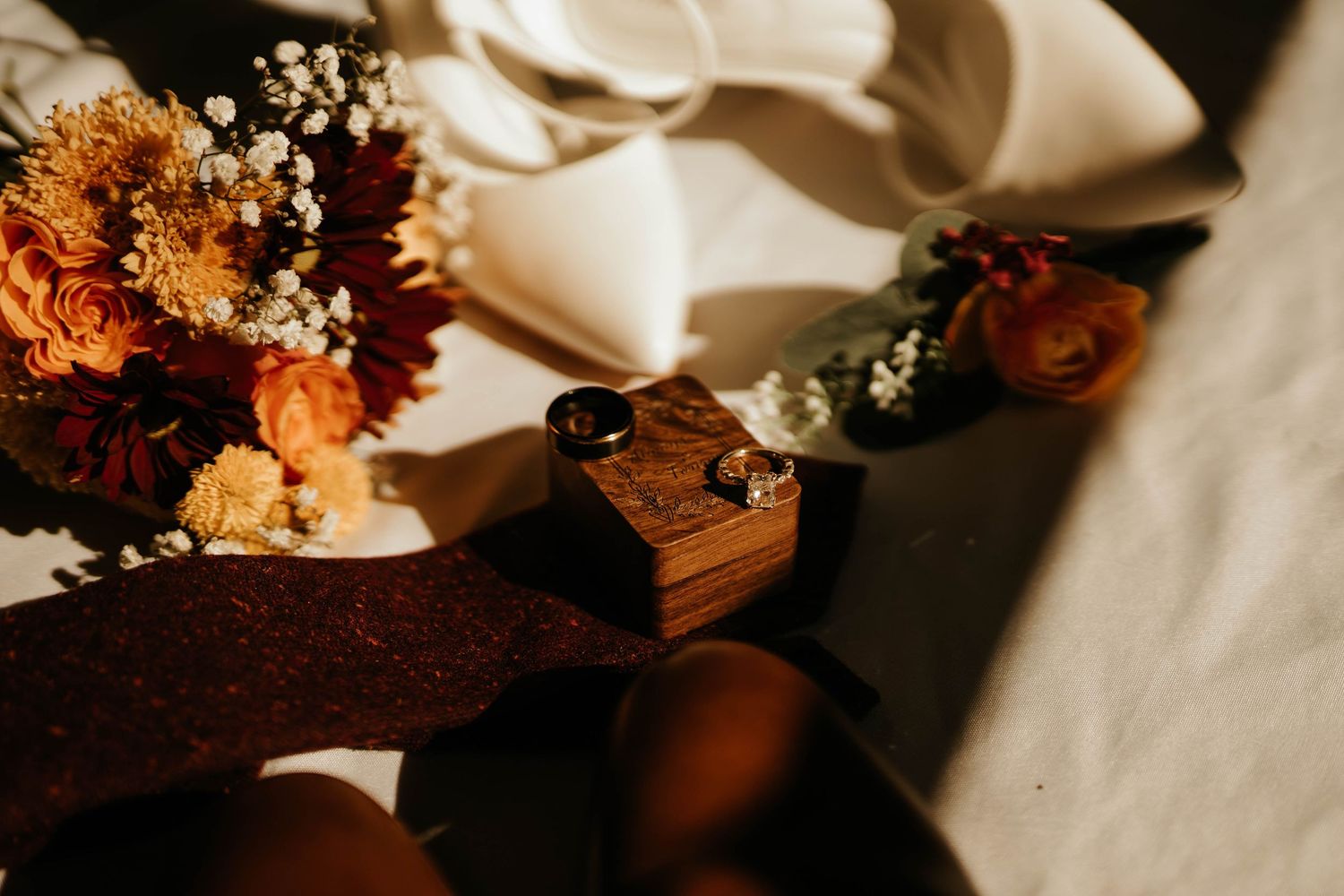 Wedding rings and autumn flowers arranged on a white cloth in warm sunlight.