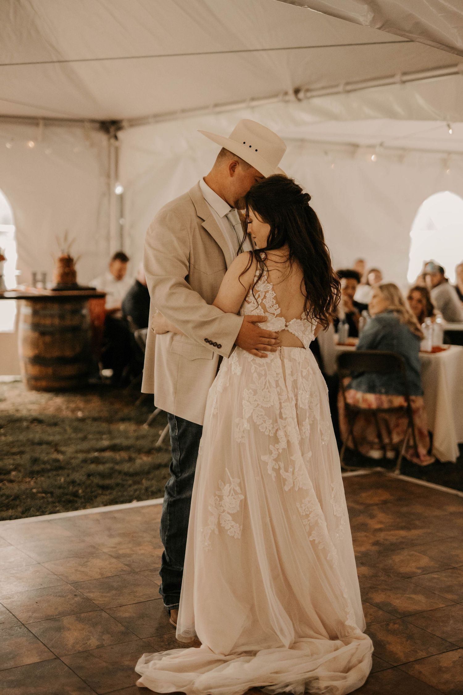A couple shares their first dance under a reception tent during their rustic outdoor wedding celebration.