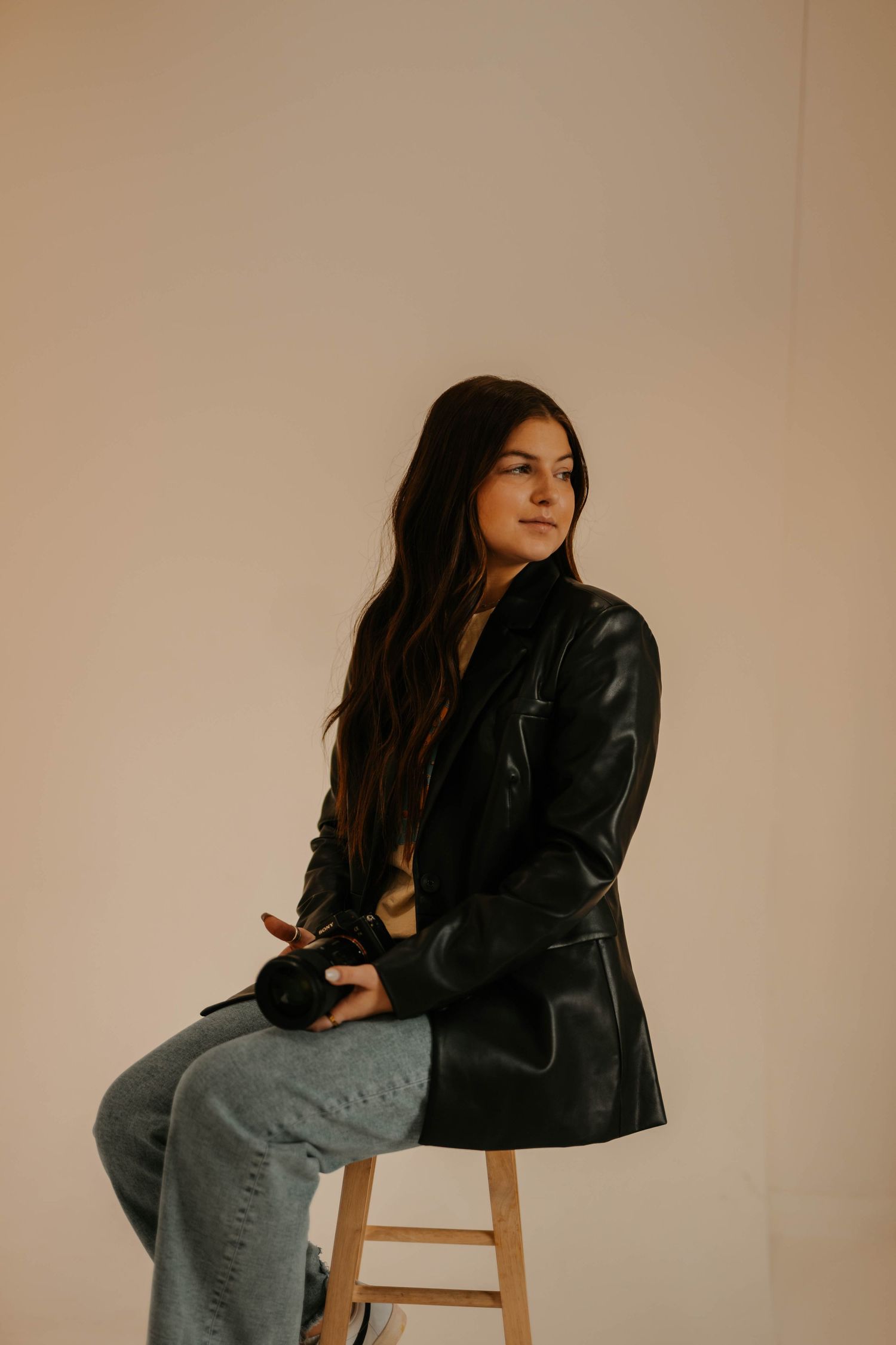 Fashion portrait series featuring leather jacket and casual styling against warm studio backdrop.
