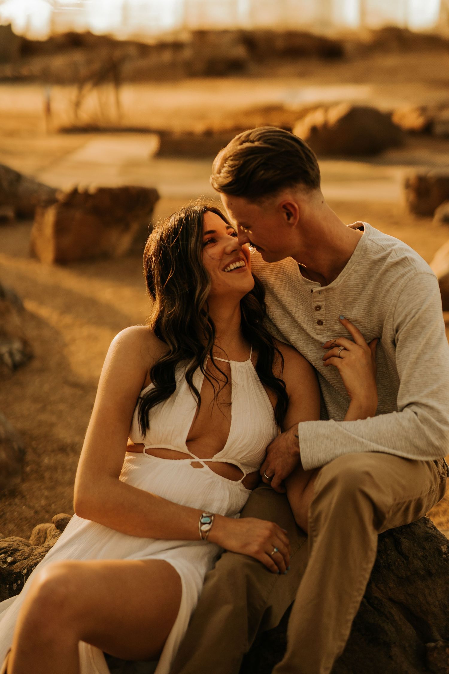 A couple shares a romantic moment at golden hour, the woman in a white dress laughing as the man leans in close.