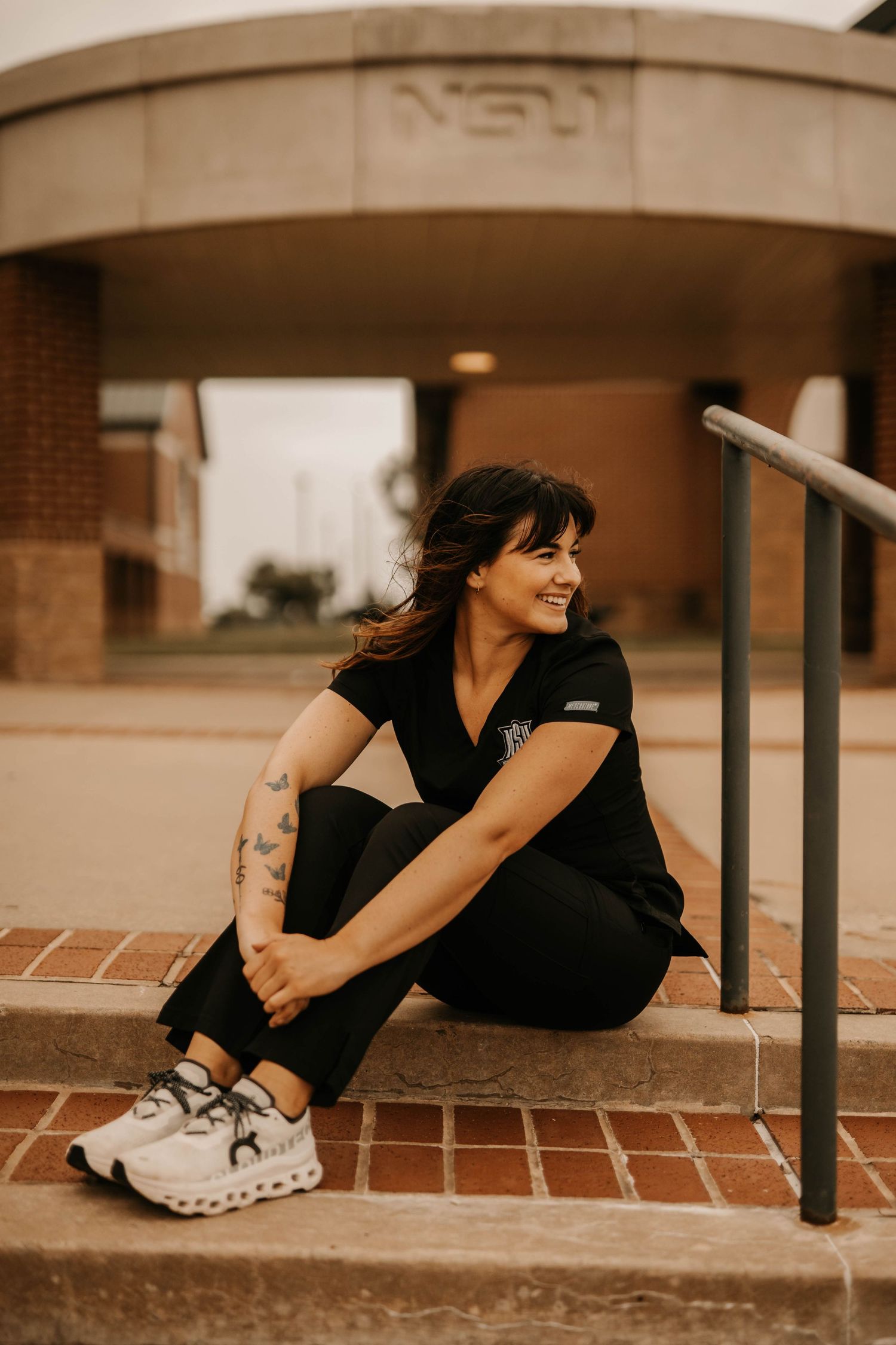 Person in athletic wear sits on brick steps with tattooed arm visible.