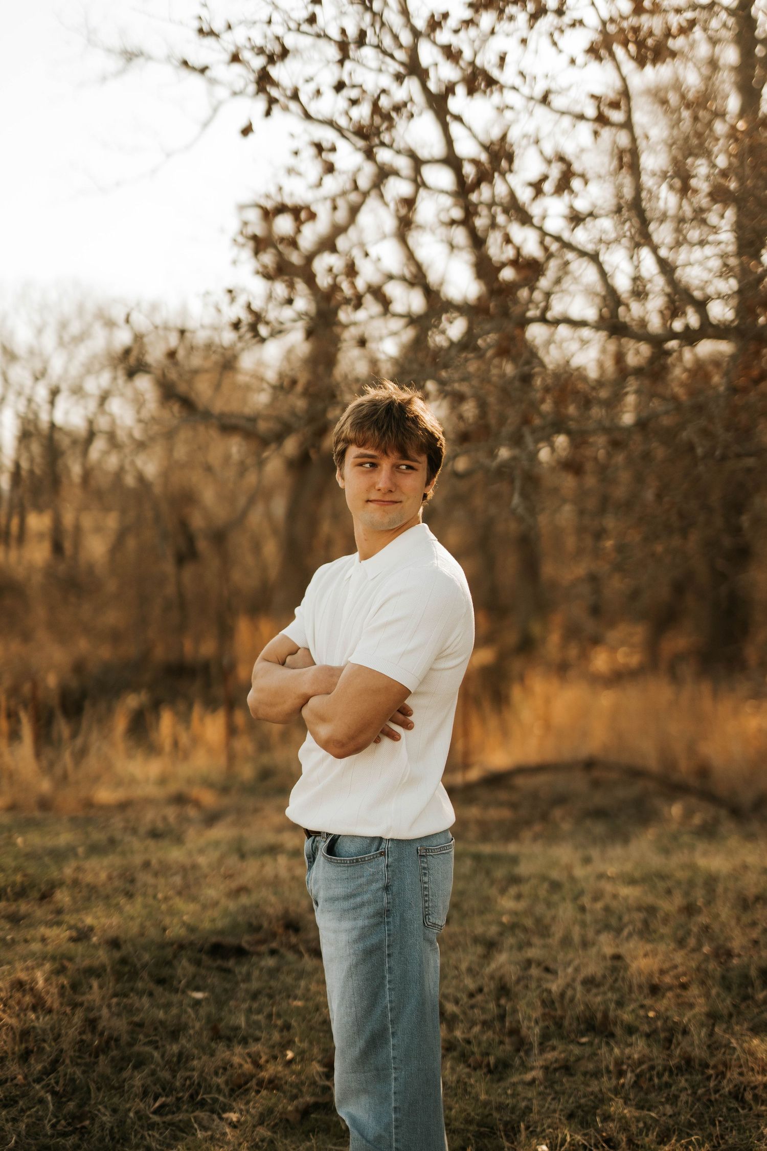 Student in white t-shirt and jeans poses against autumn background.
