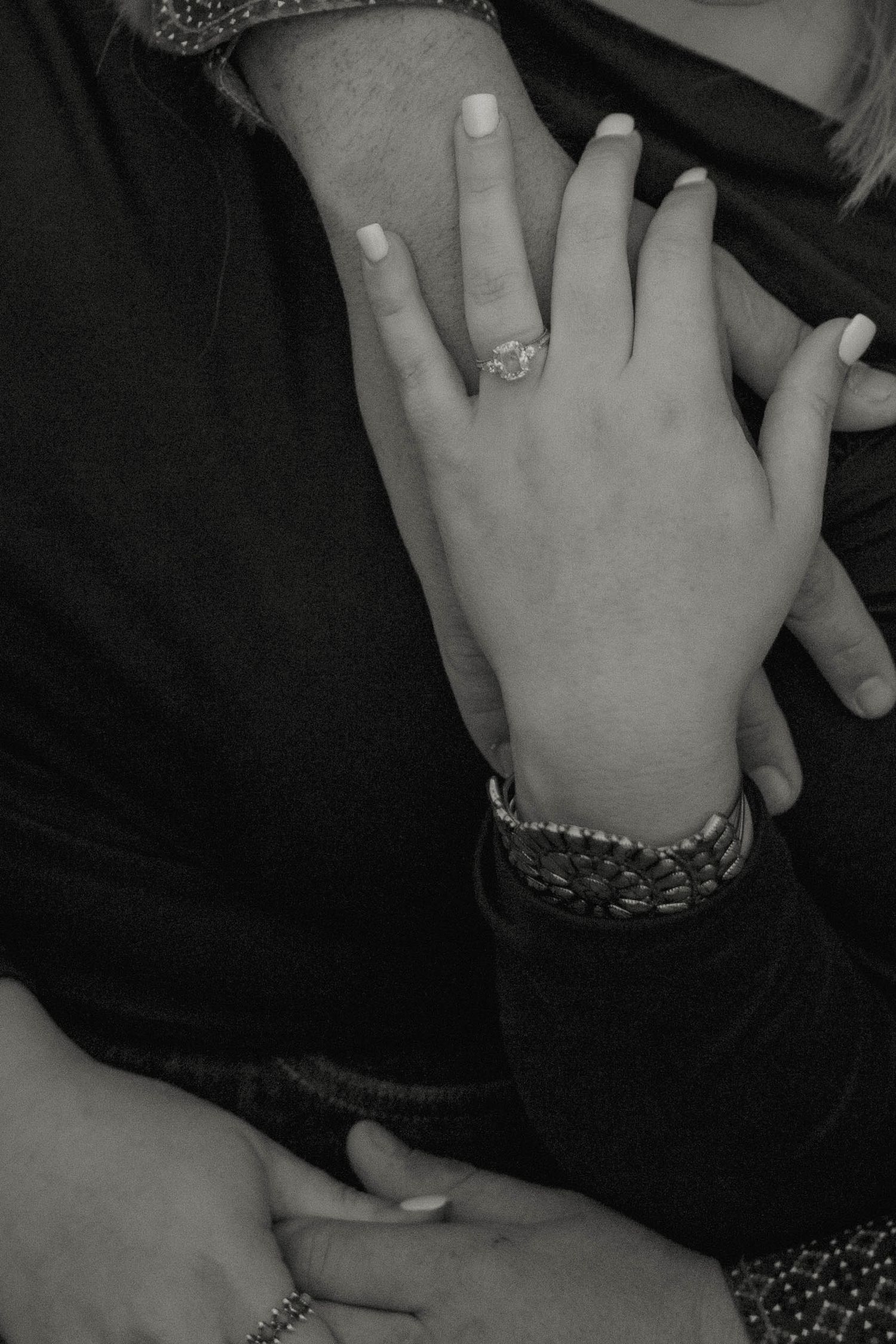 Close-up black and white photo of hands with engagement ring and bracelets.