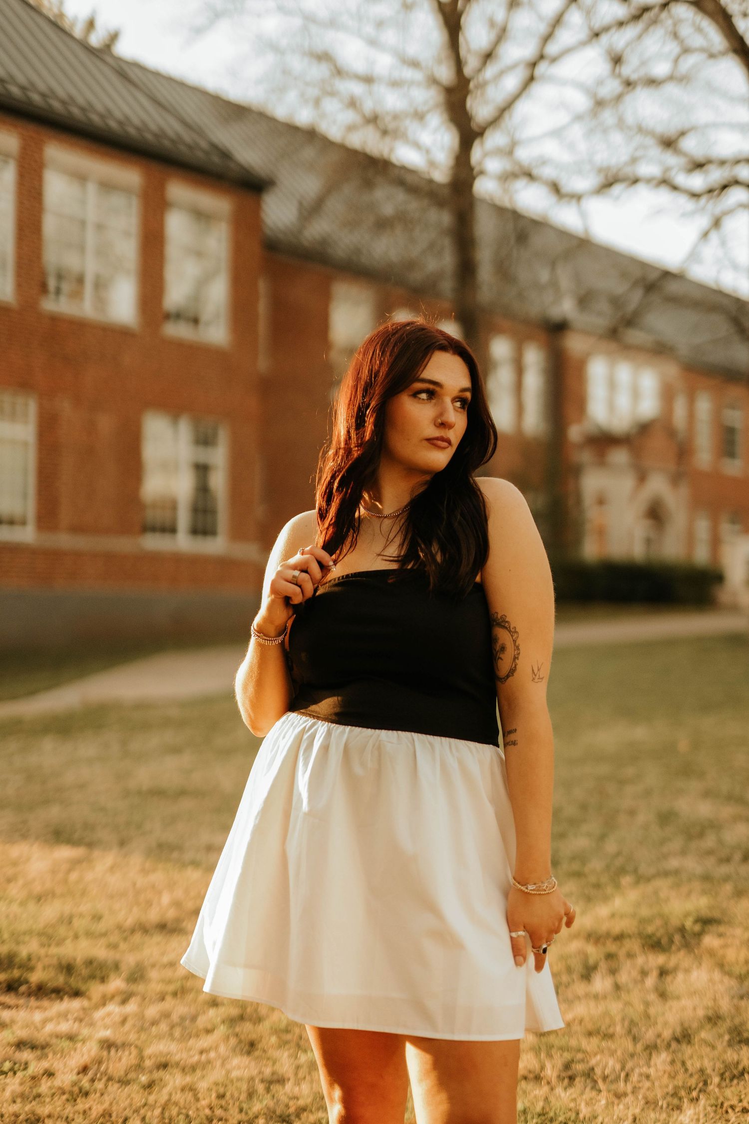 Student in black and white outfit poses in front of brick university building at sunset.