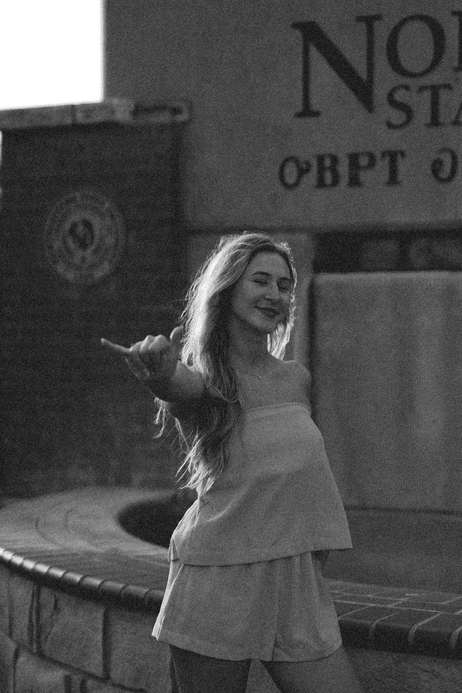 A black and white photo captures someone in a flowing dress spinning joyfully outdoors.