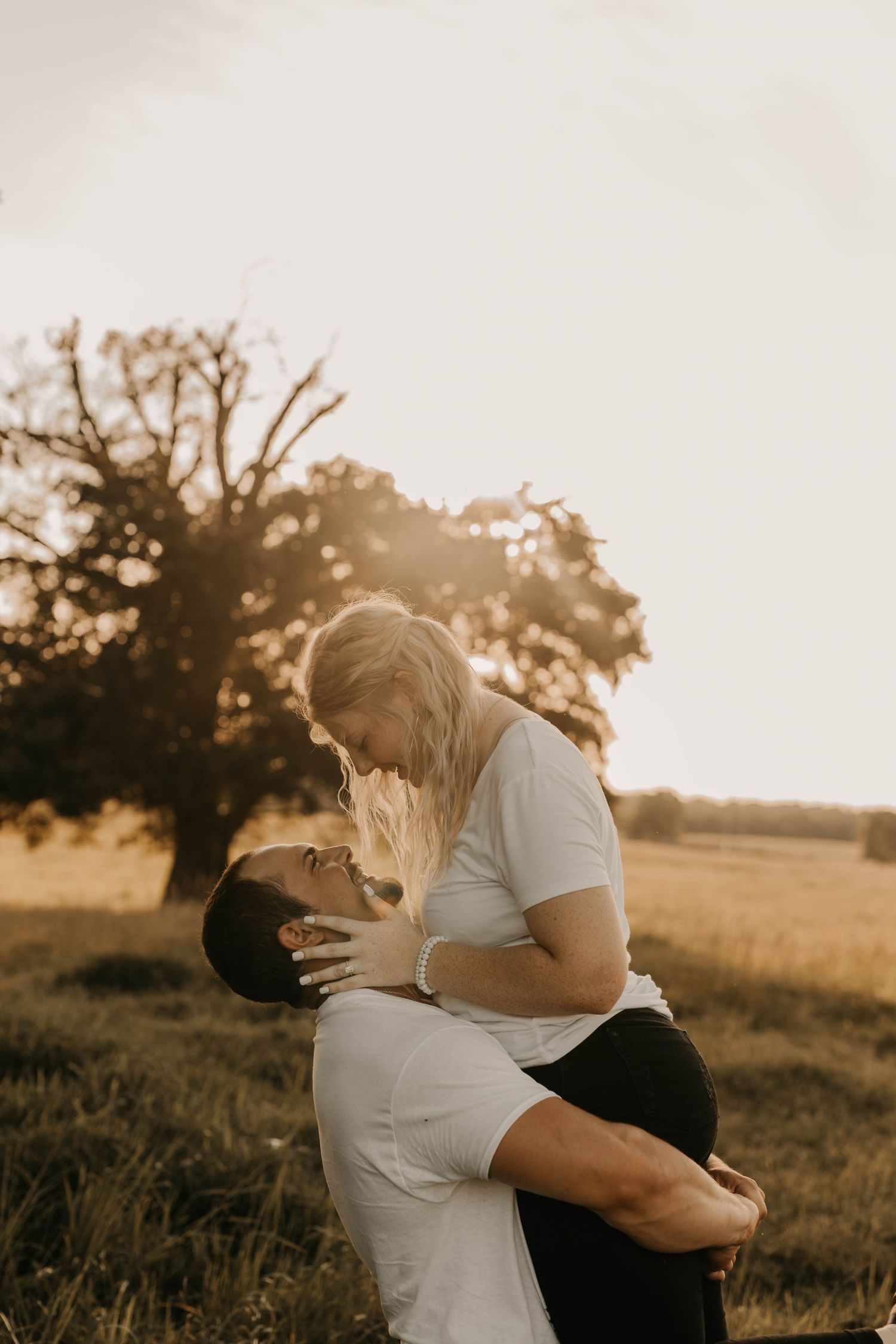 Couple embracing passionately in a sunset-lit field with trees in the background.