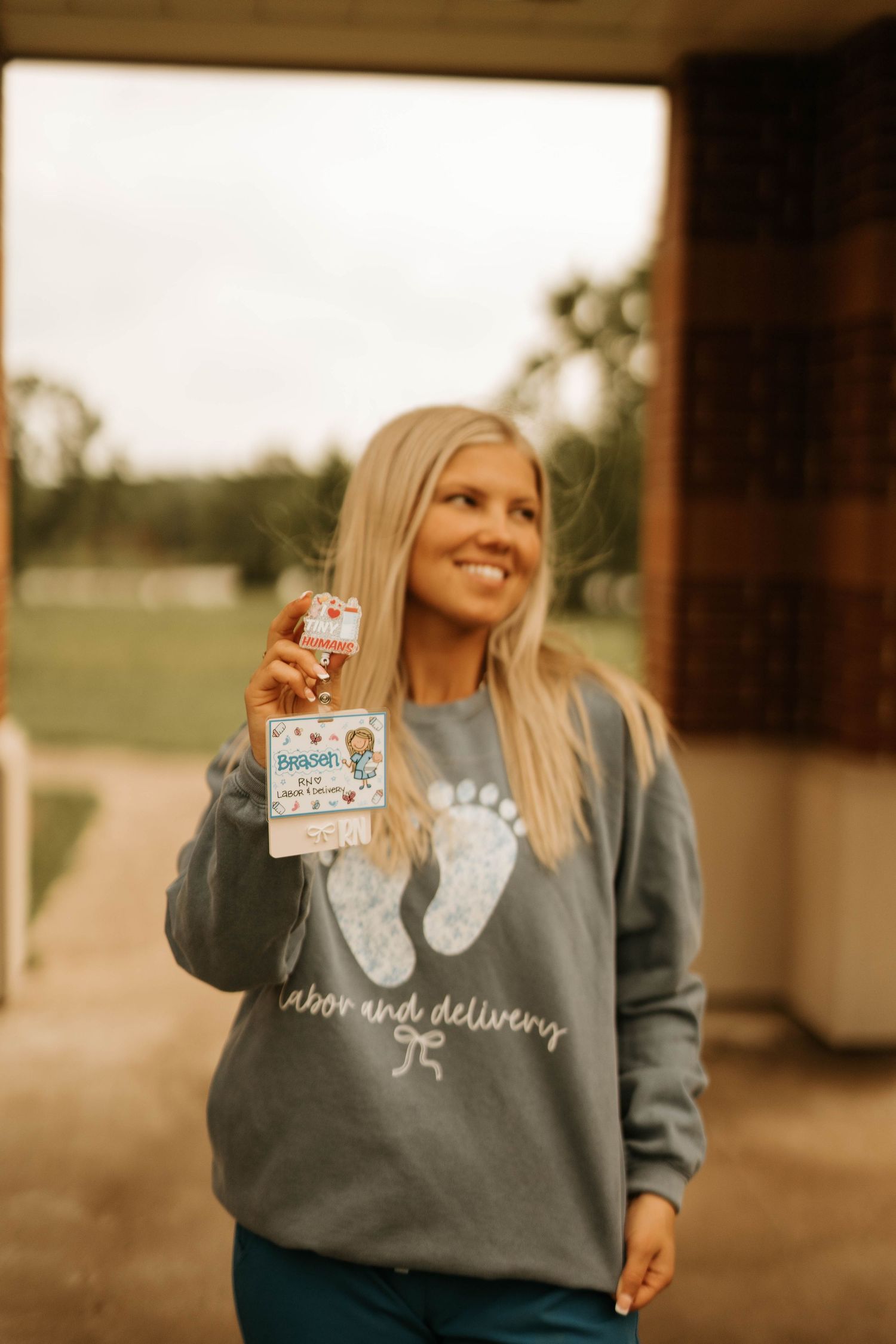 Healthcare worker displays ID badge while wearing gray footprint-themed sweatshirt.