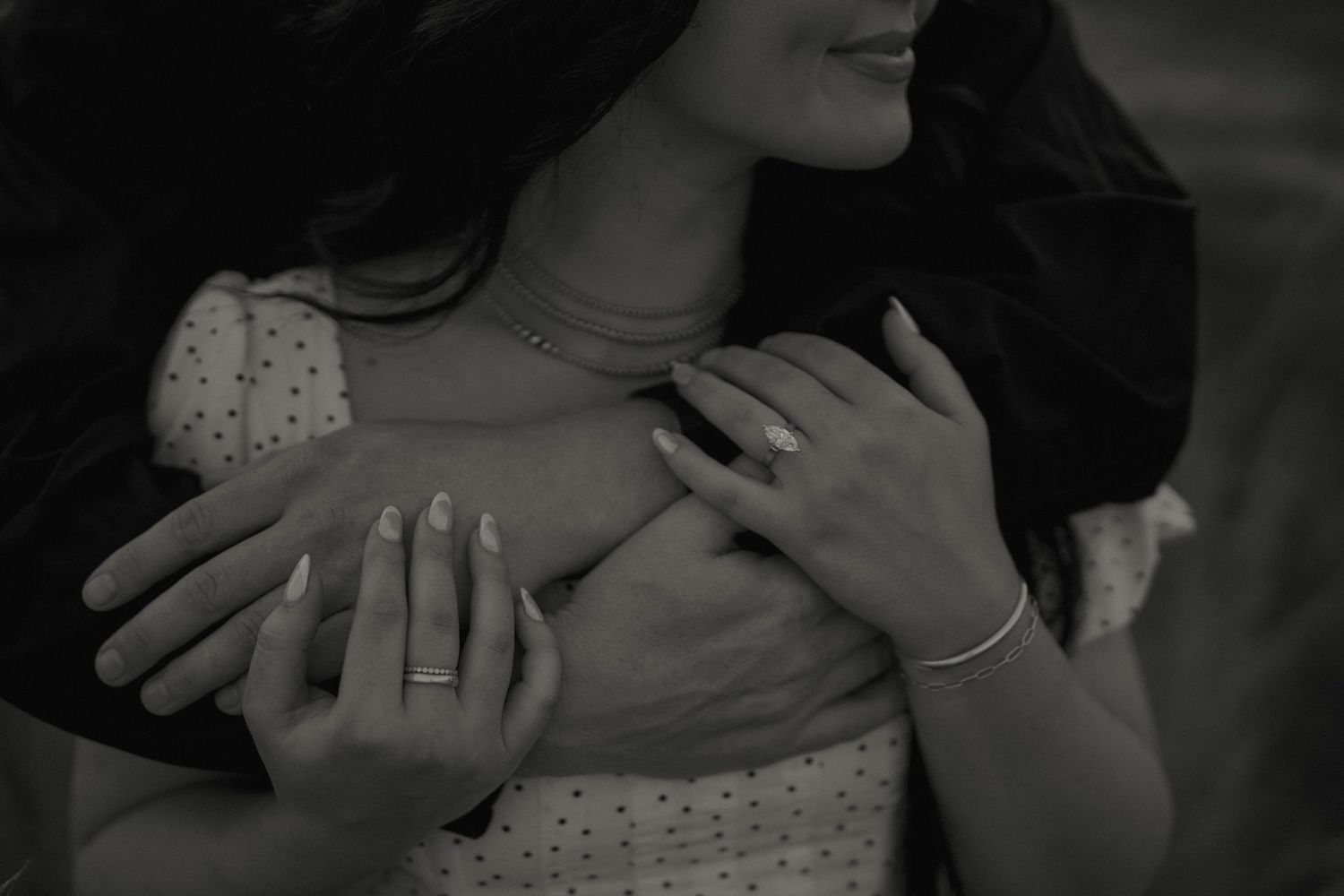 Close-up black and white photo of hands wearing polka dot sleeves and delicate jewelry.
