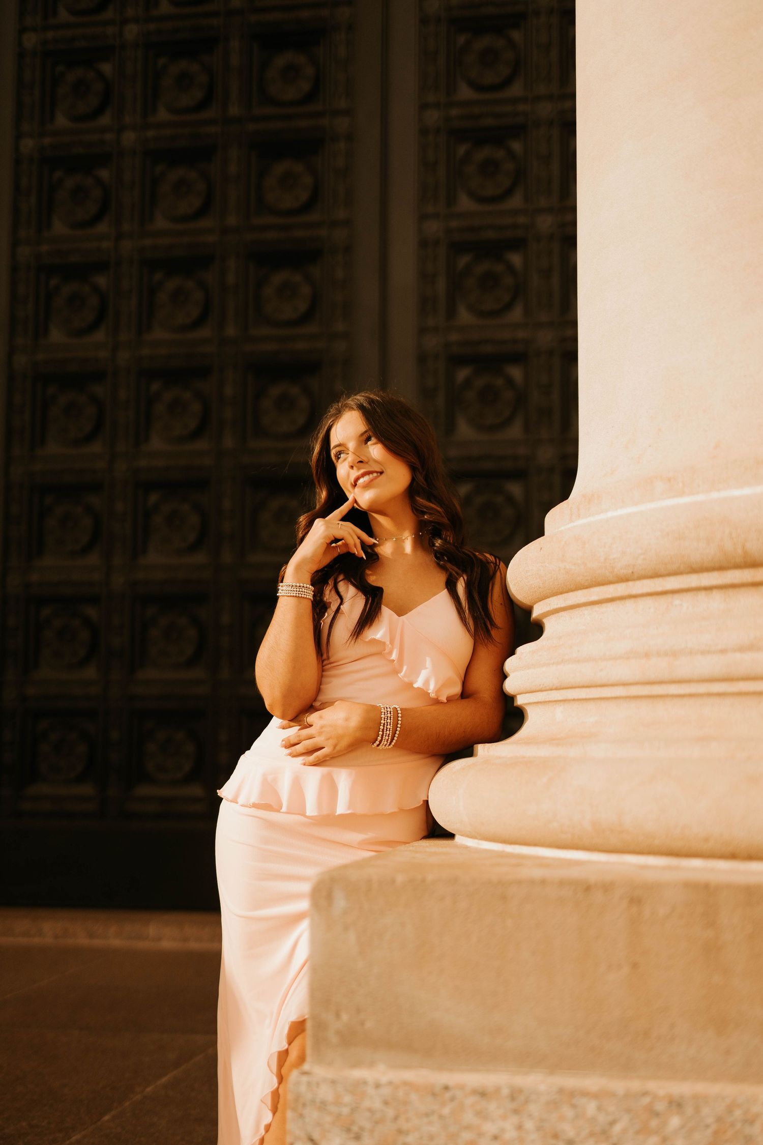 Woman in pink dress posing elegantly against ornate architectural details.