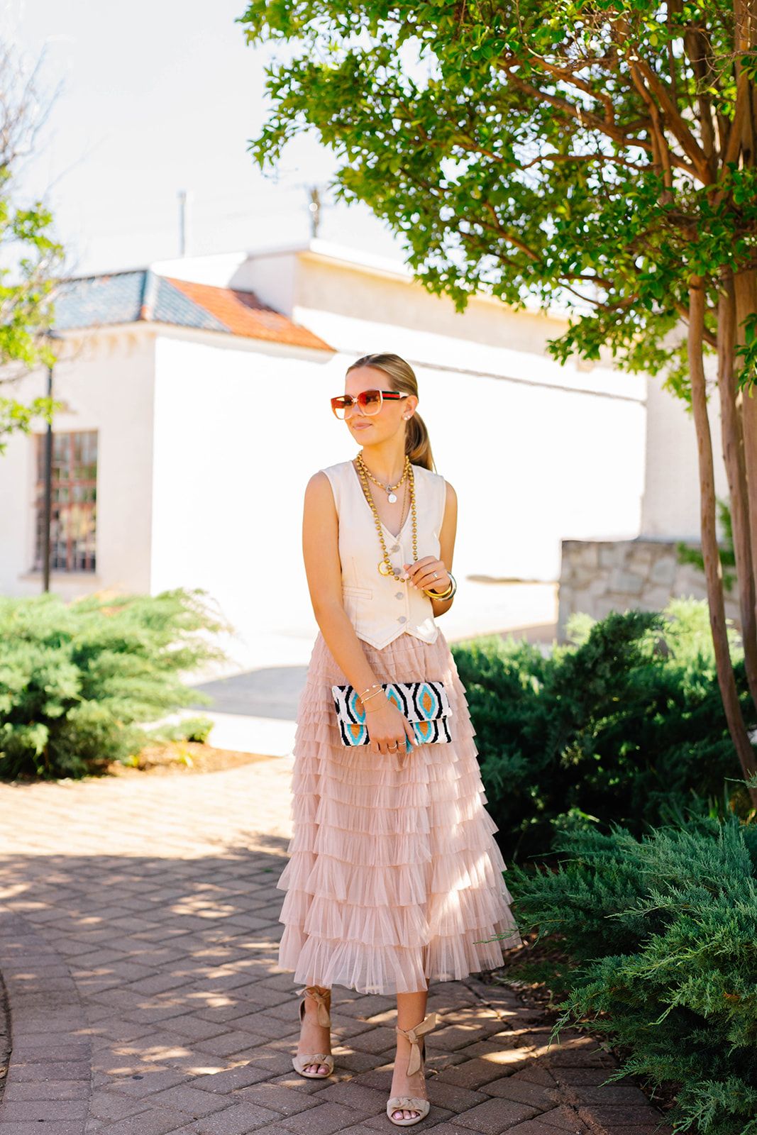 Garden path fashion with tiered pink skirt and cream sleeveless top under leafy trees.