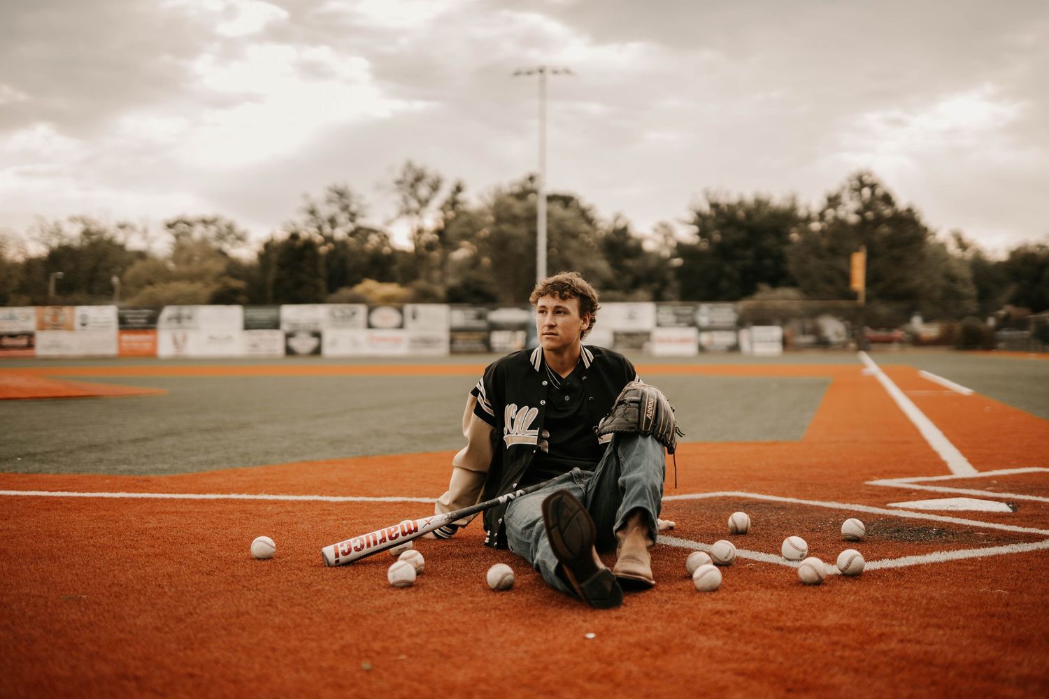 Baseball player sitting on field with equipment scattered around during practice session.
