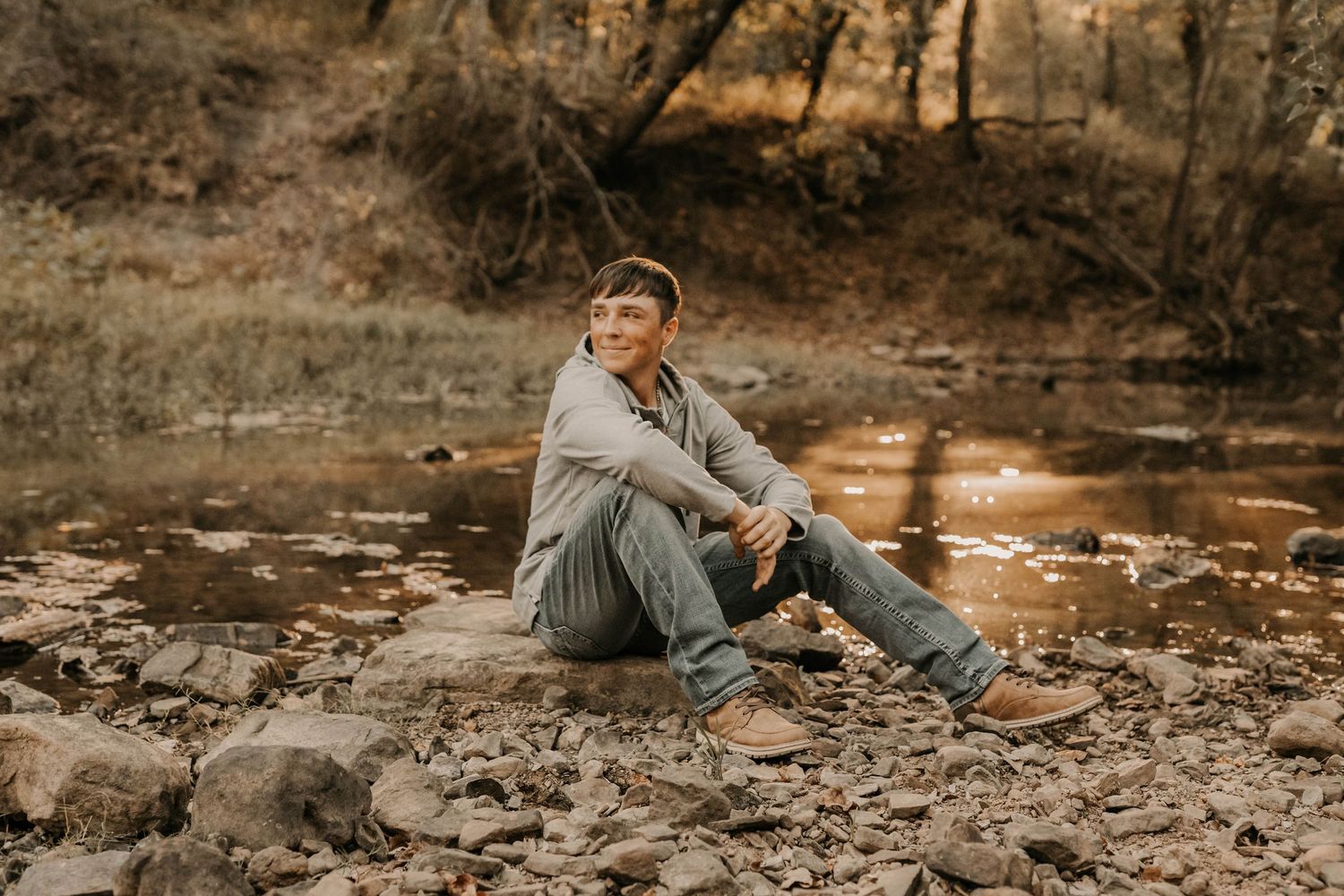 Person sitting on rocky creek bed during golden hour photography session.