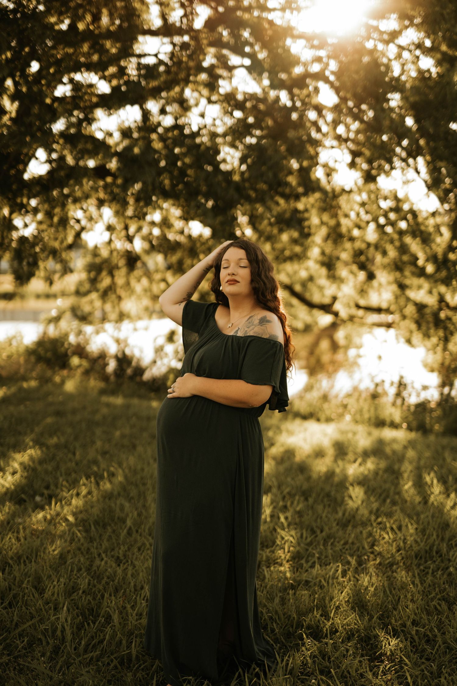 A person in a black maxi dress poses in golden sunlight under tree branches.