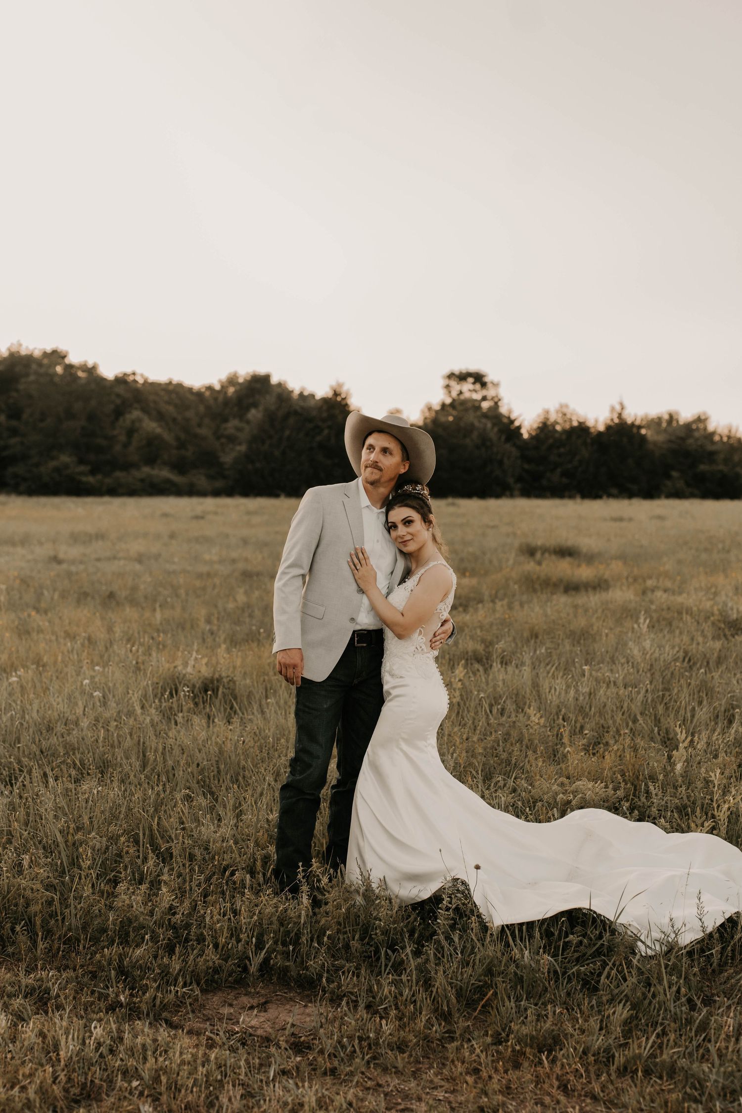 Cowboy-themed wedding portrait with couple posing in field at golden hour.