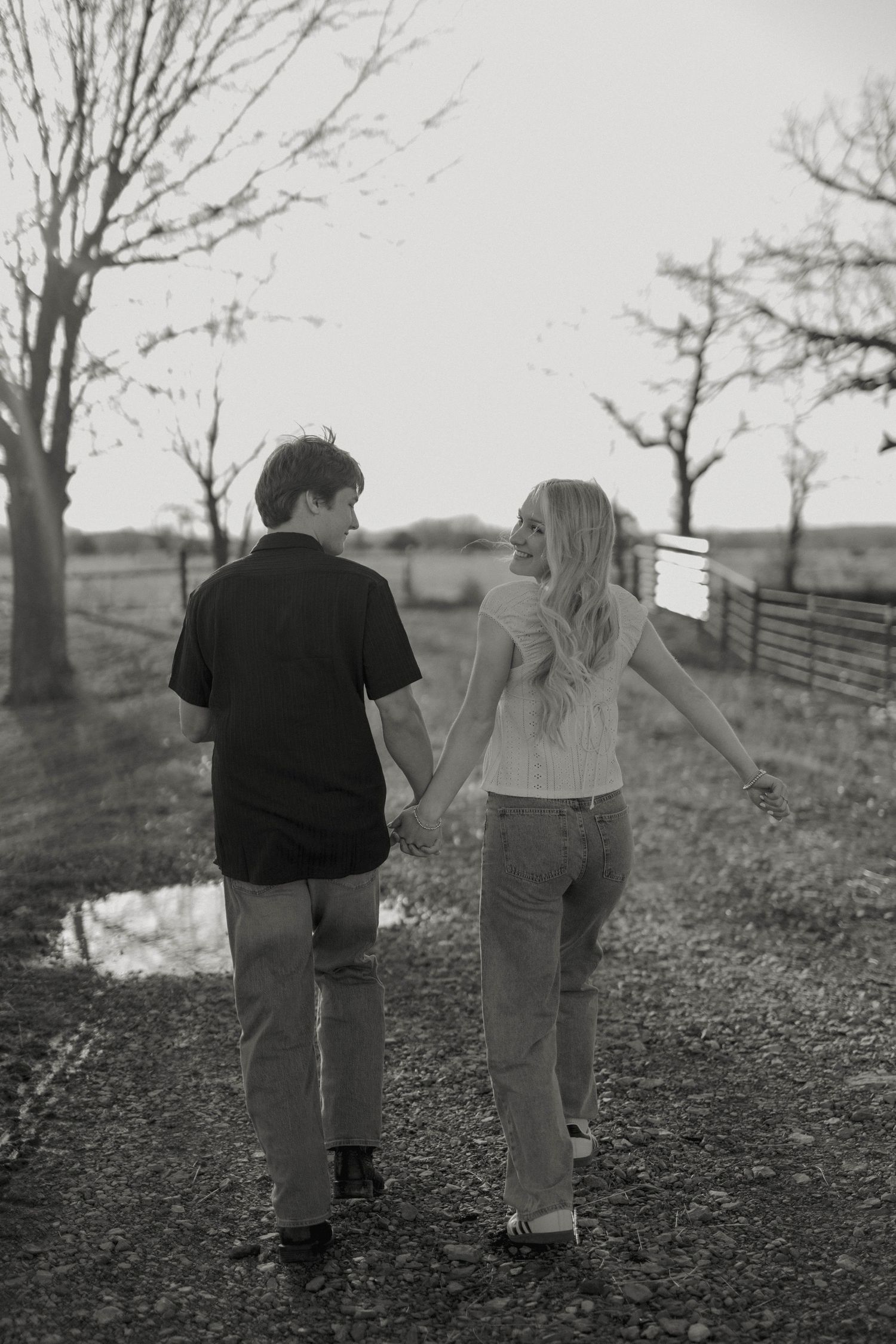 Black and white photo of couple walking hand in hand through rural landscape.