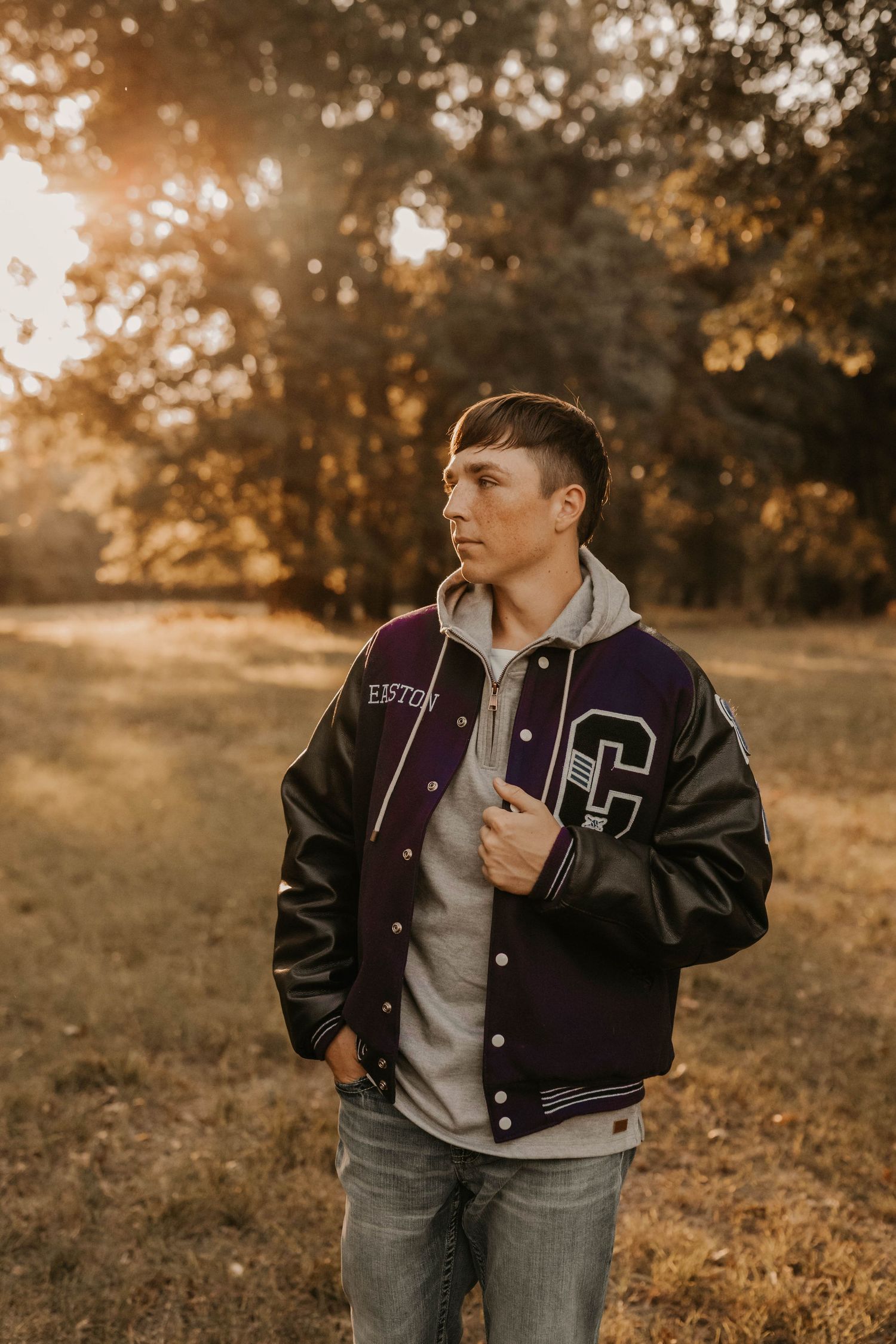 Person wearing varsity letterman jacket and hoodie in autumn setting with golden light.