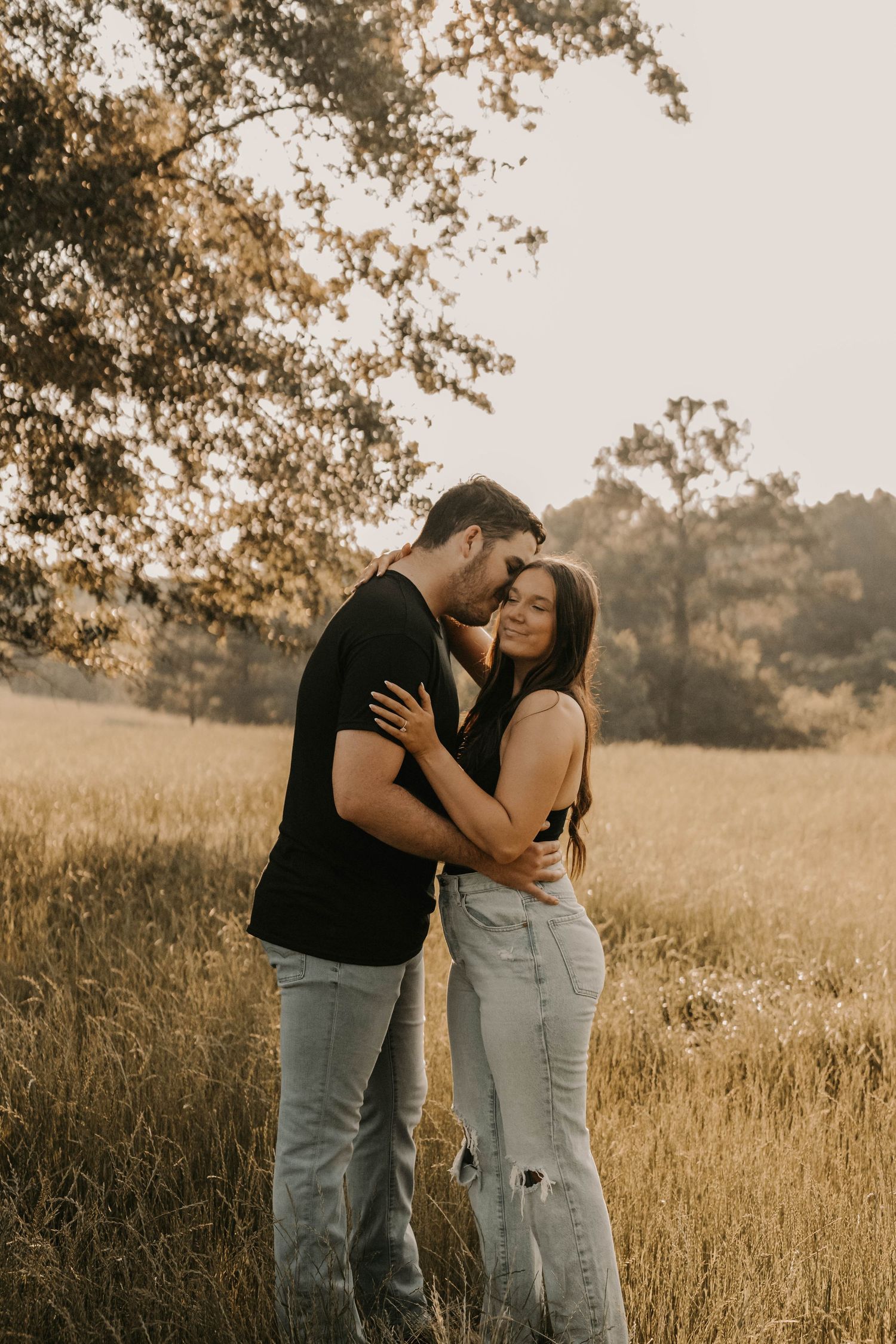 Couple embracing in casual wear during golden hour in a rustic field setting.