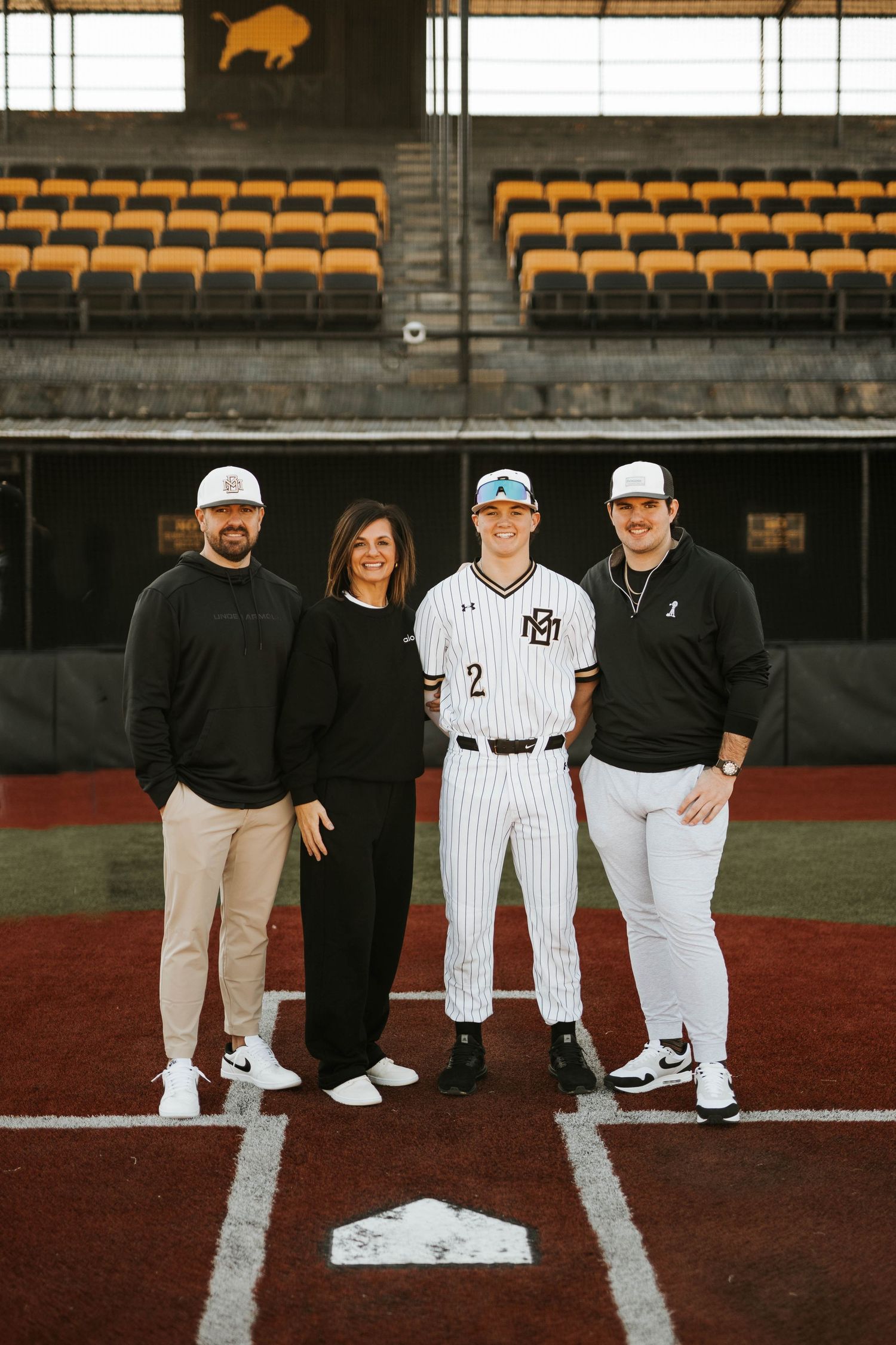 Baseball family photo on home plate with player in striped uniform and stadium seating in background.