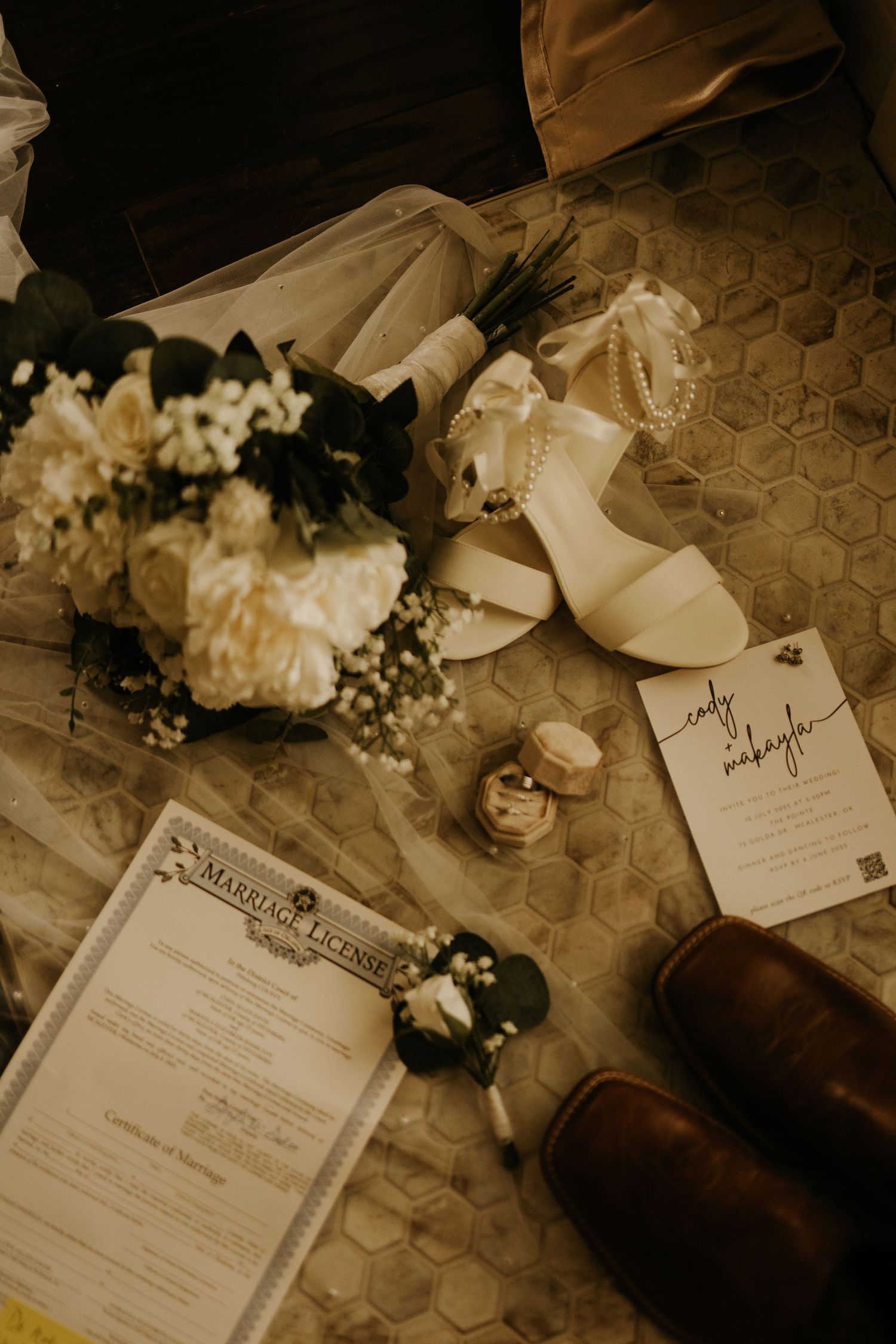 Wedding flat lay with marriage license, bridal bouquet, white heels, cowboy boots, and stationery on marble tile.