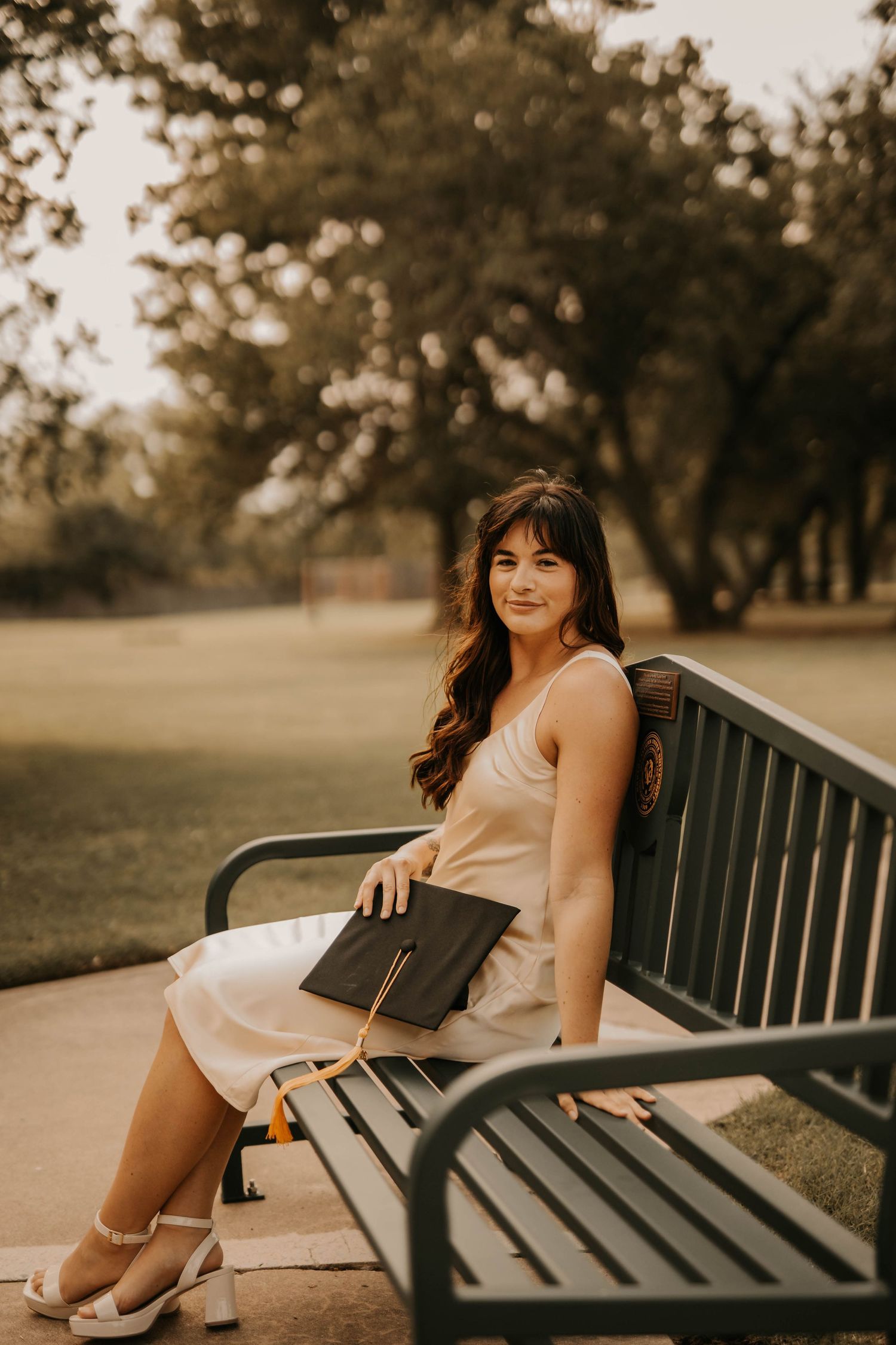Woman seated on a park bench holding a folder on a warm autumn day.