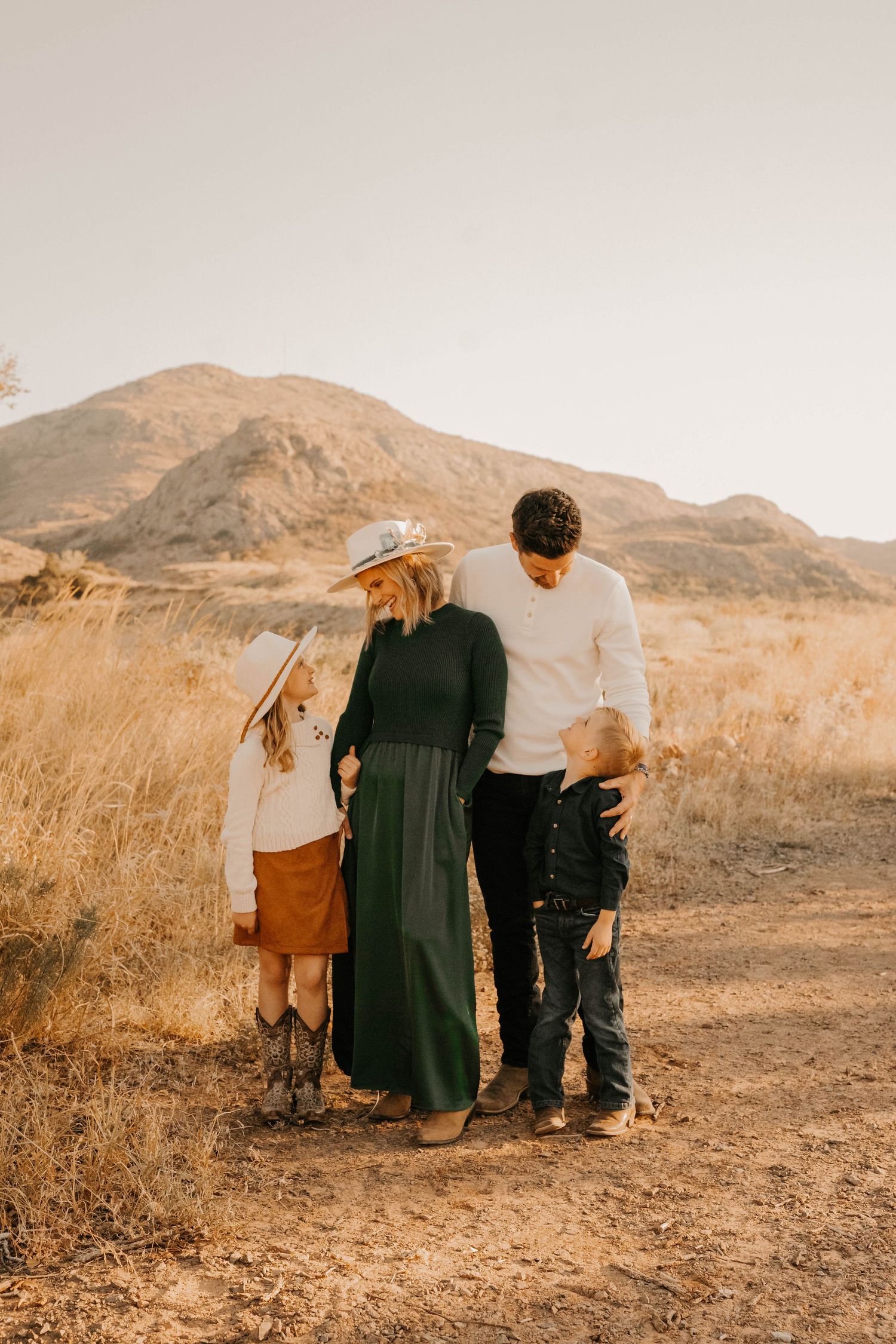 Couple stands together against desert mountain backdrop in warm sunset light.