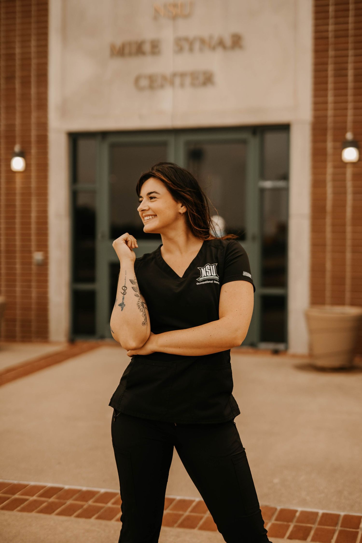 Person in black uniform smiles outside Mike Synar Center building.