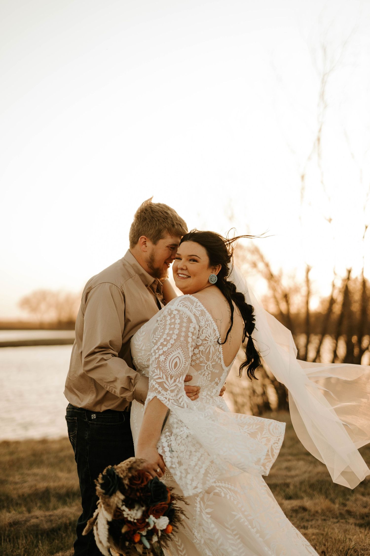 Wedding couple shares intimate moment at sunset with bride in lace dress and groom in casual attire.