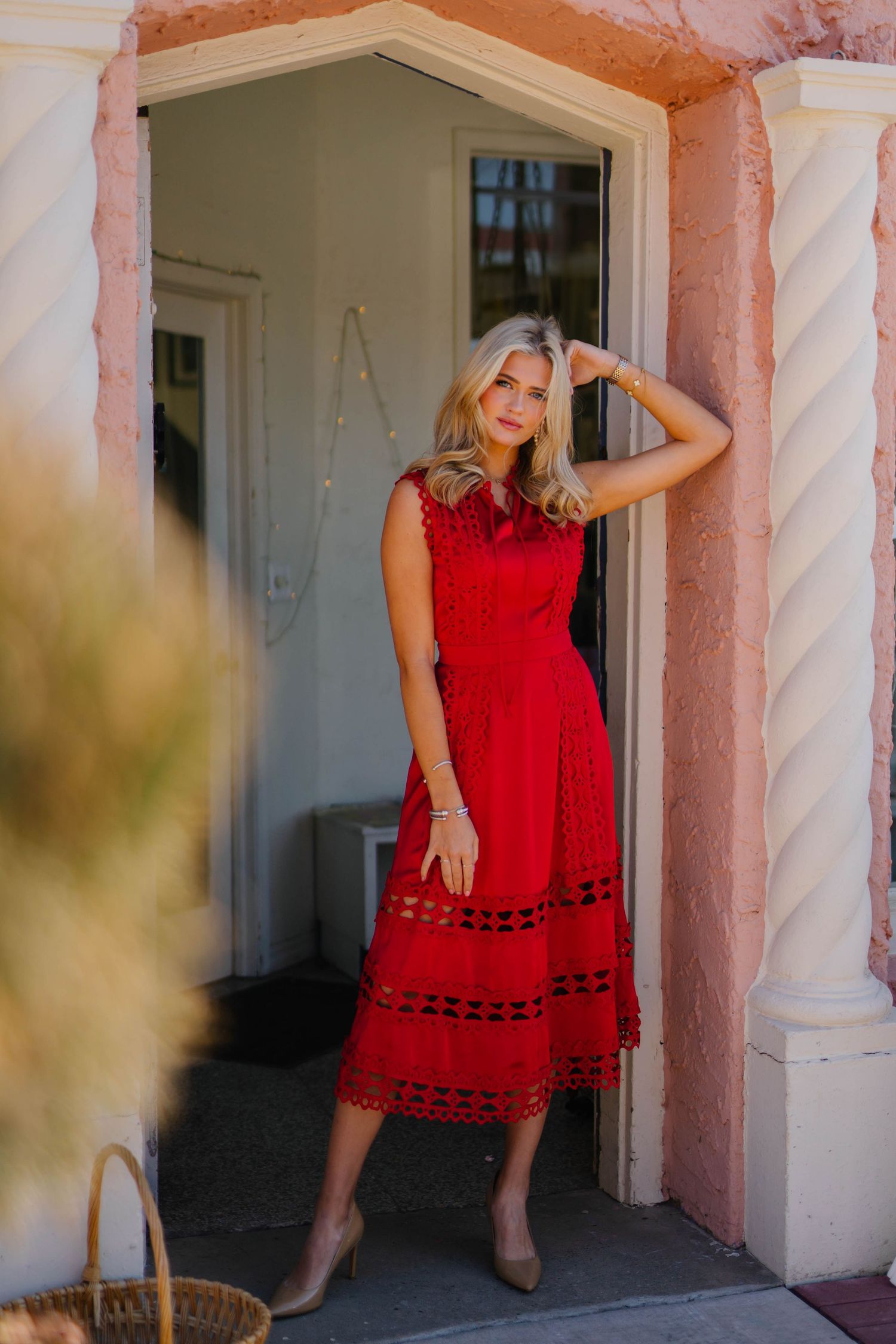 Elegant red lace dress worn in doorway of pink Mediterranean-style building.
