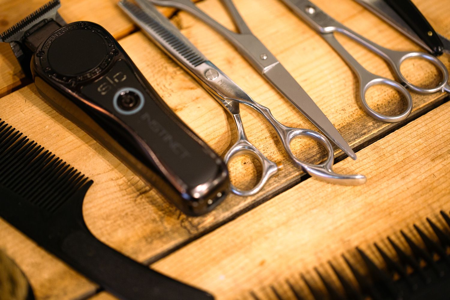 Professional barber tools including scissors, combs, and clippers arranged on a wooden surface.
