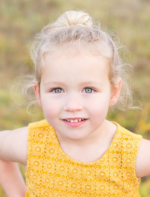 Close-up portrait of a young child with light hair and bright eyes wearing a yellow patterned top.