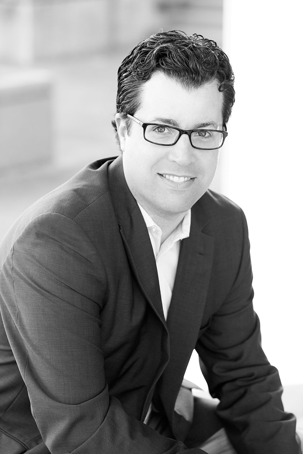 Black and white professional headshot of businessman in glasses and suit.