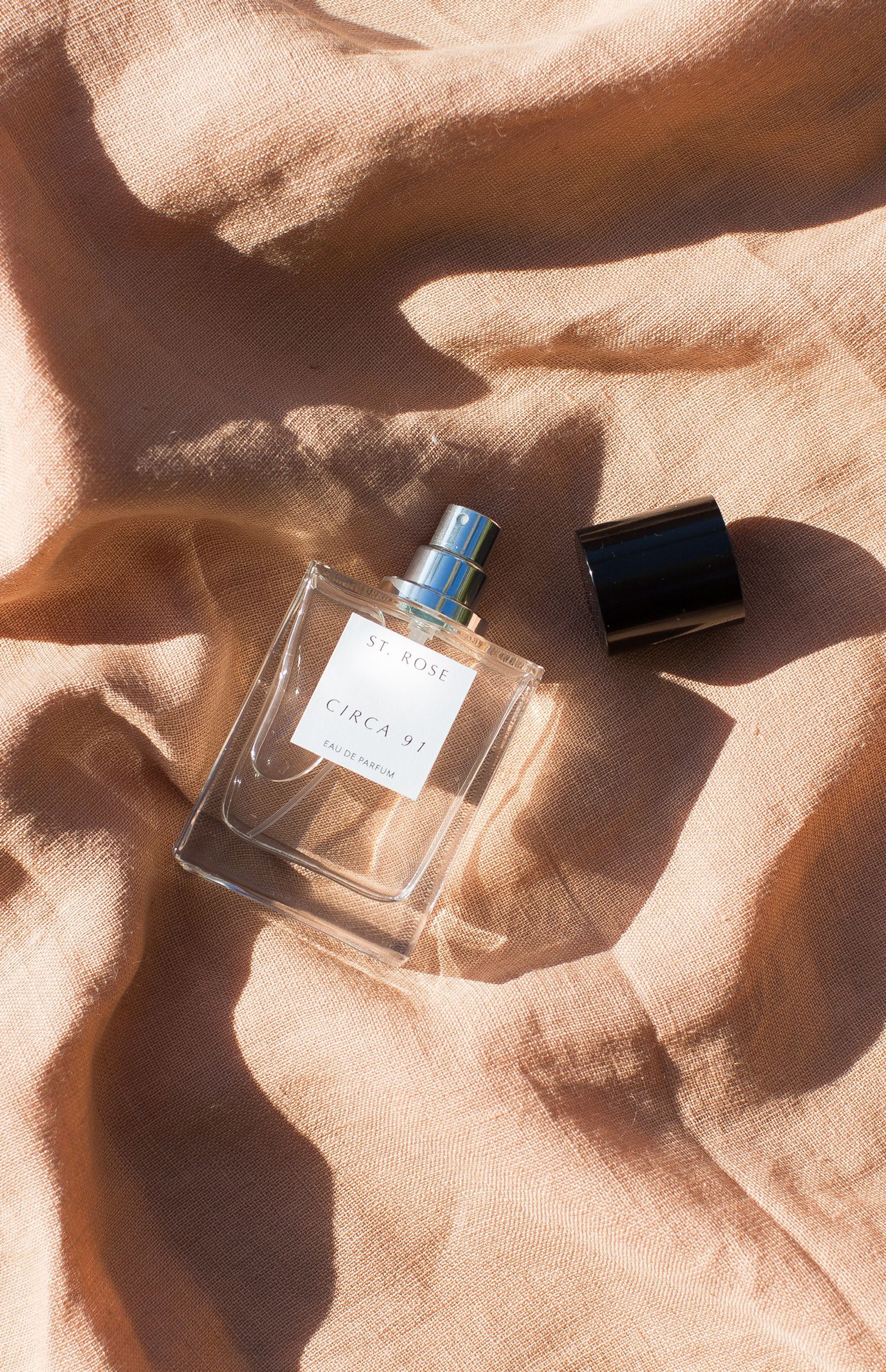 Glass perfume bottle on peach-colored fabric with dramatic shadows.