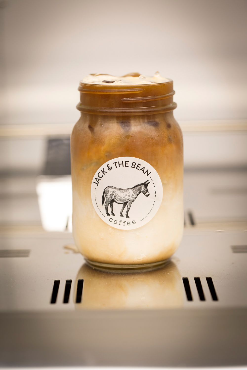 Mason jar filled with iced latte bearing Jack & The Bean coffee shop logo.