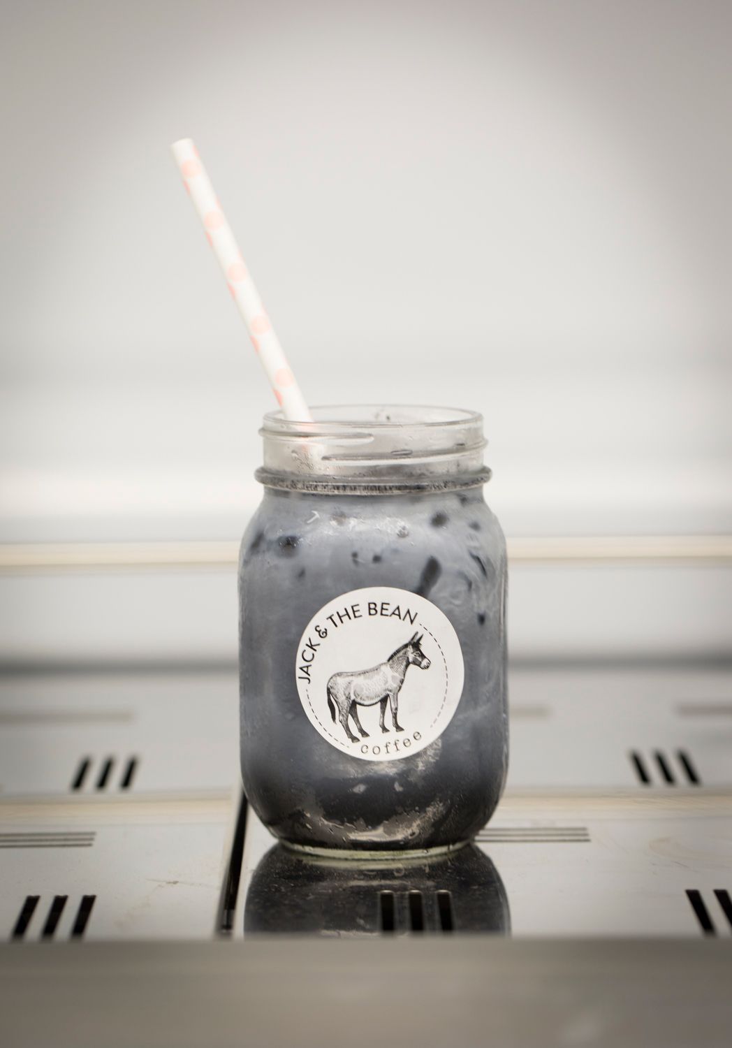 Dark iced coffee drink in mason jar with donkey logo and white straw.