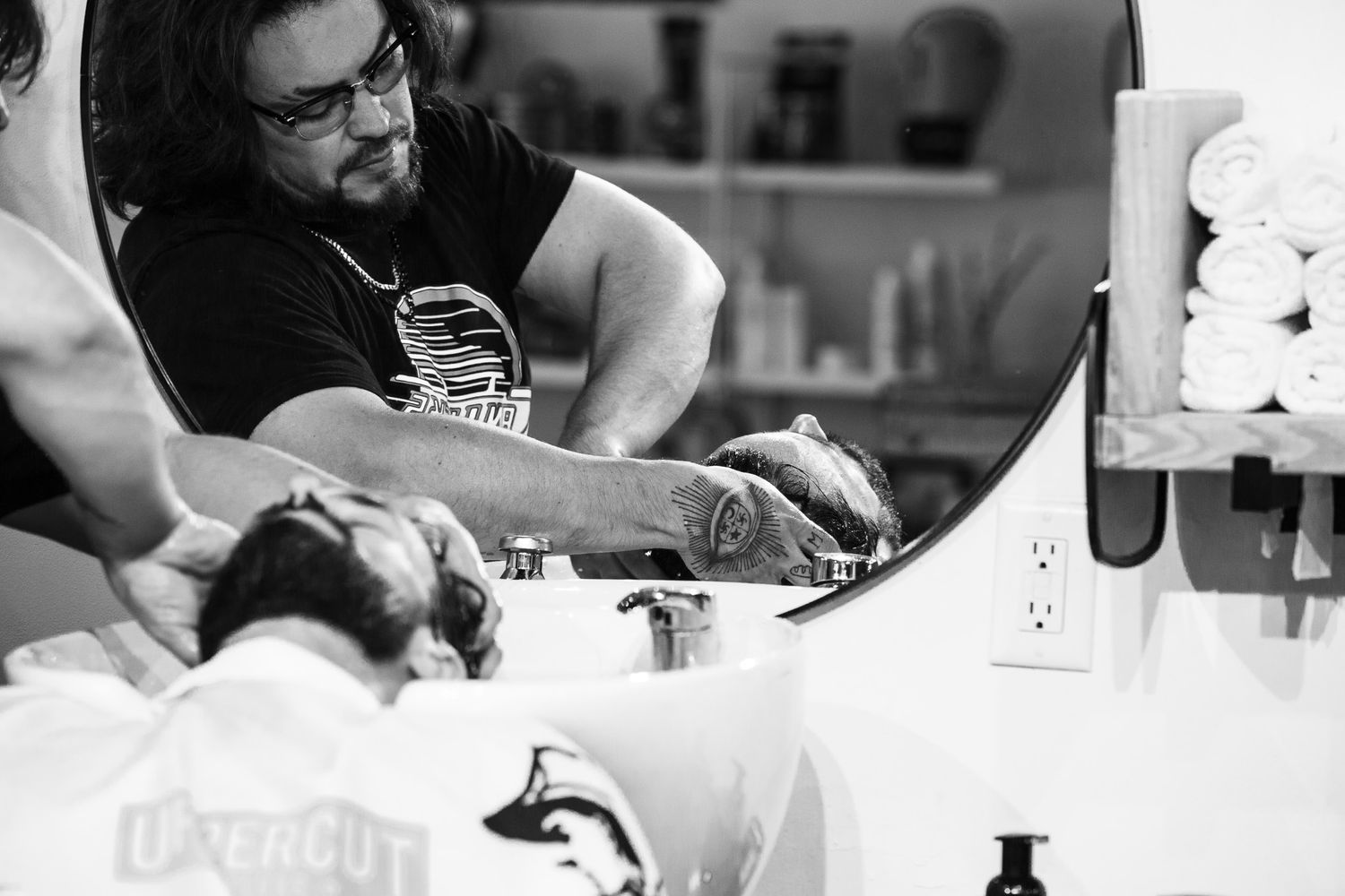 Black and white image of tattoo artist working on client in studio setting.