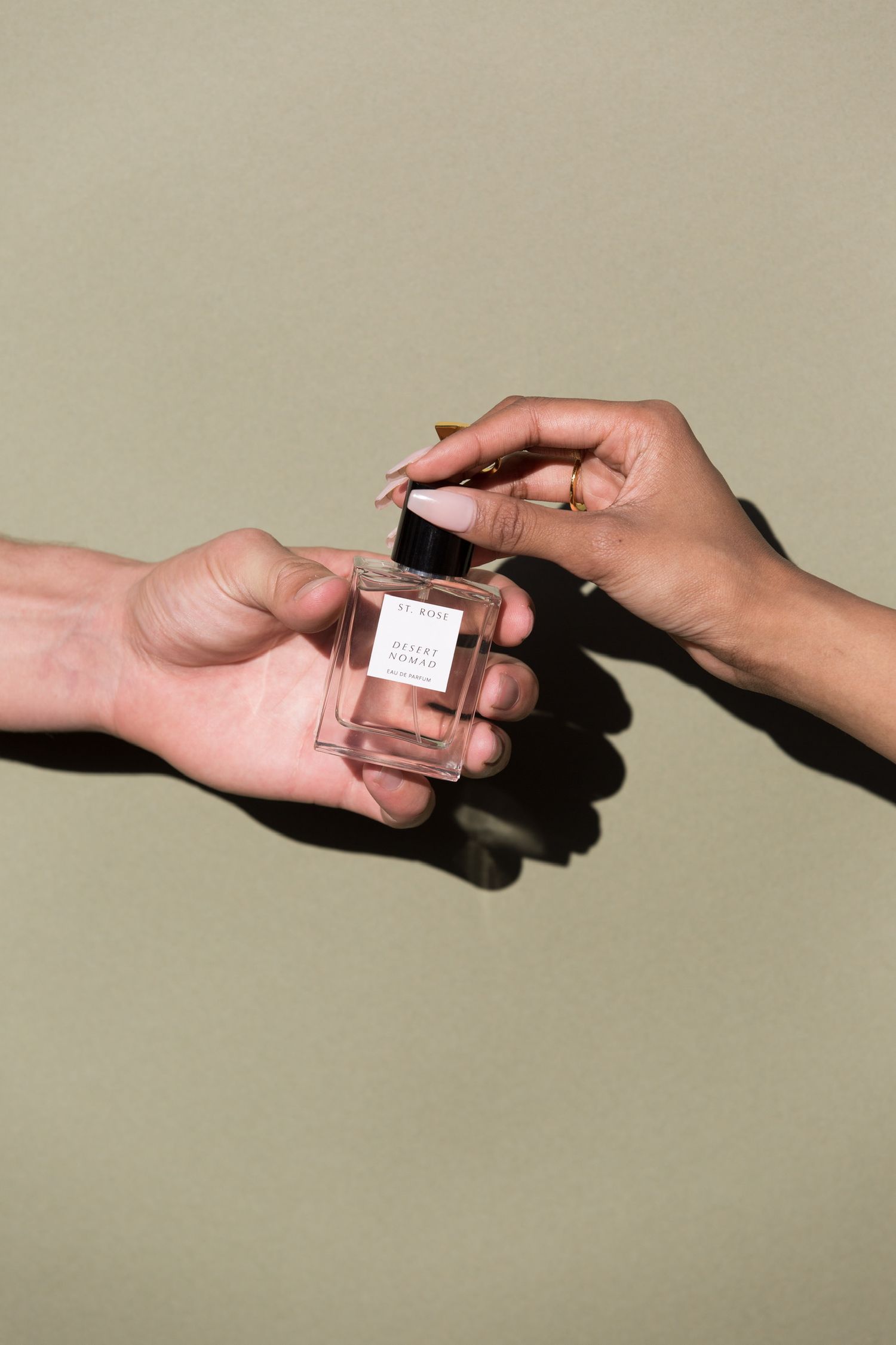 Hands passing a small perfume bottle against a neutral background.
