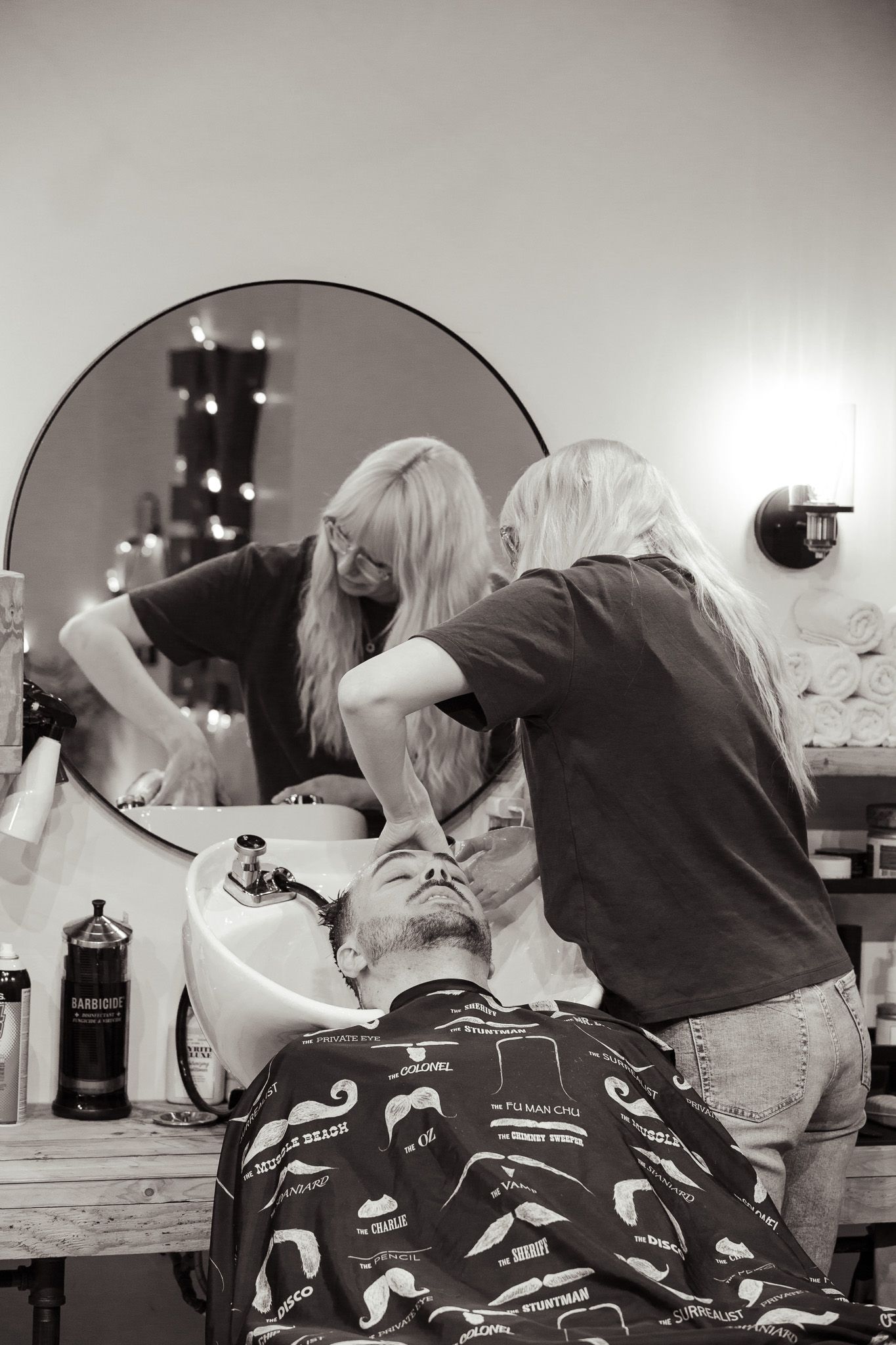 A black and white photograph of a hair washing service at a salon sink.