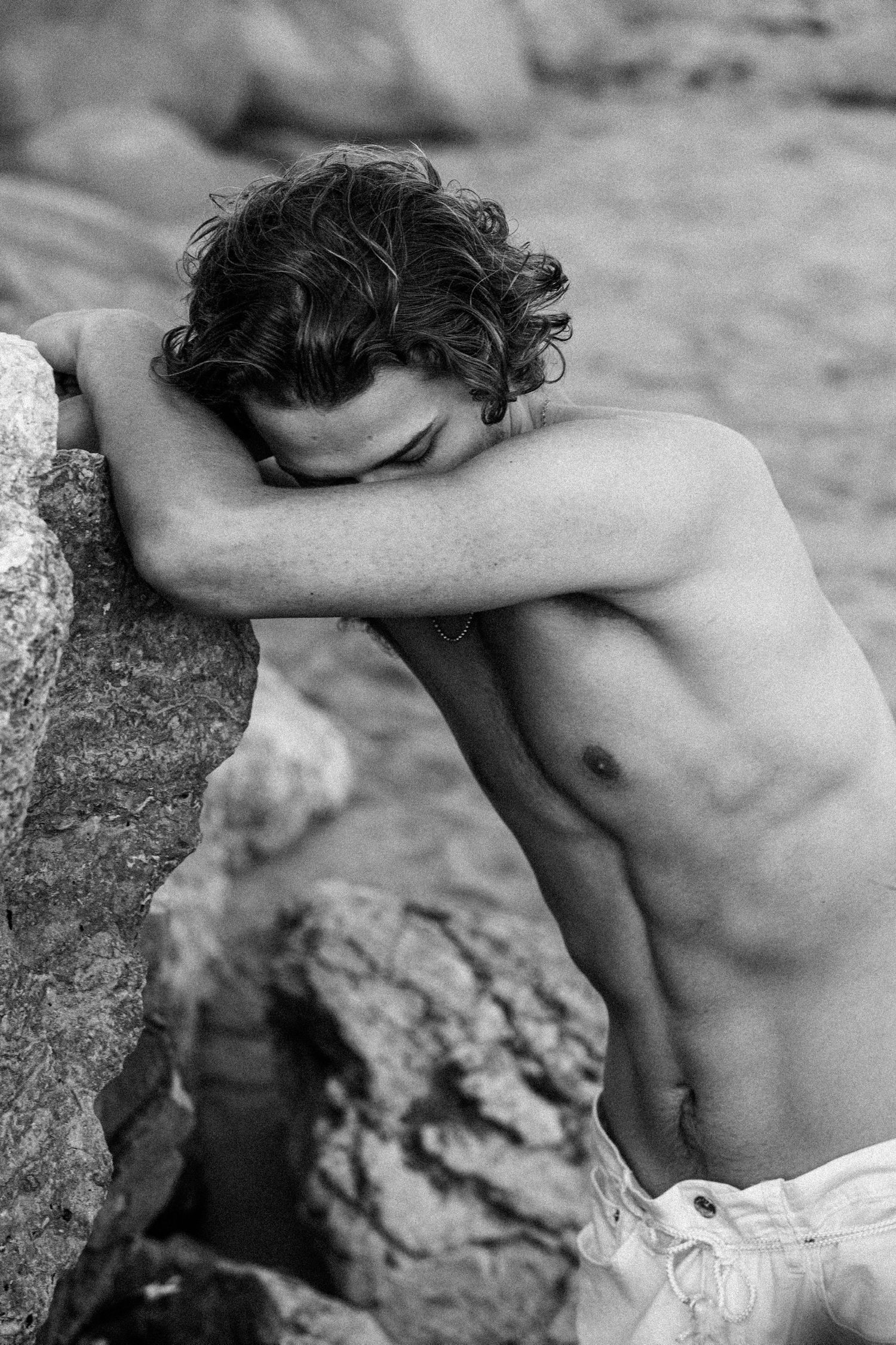 Artistic black and white photograph showing bare torso against rocky background.