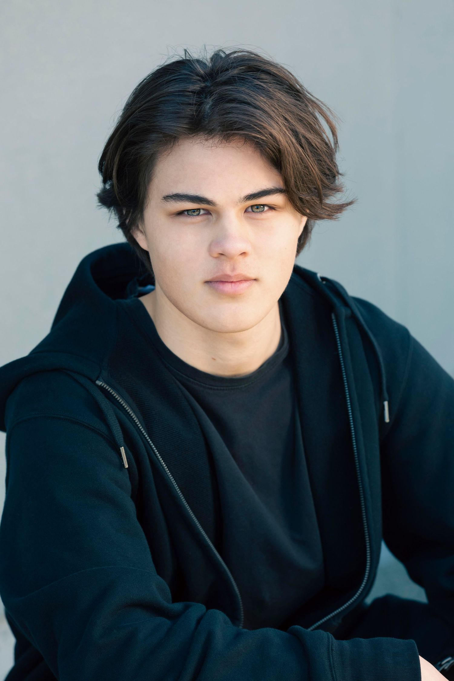 Portrait series of person in black hoodie against light gray background.