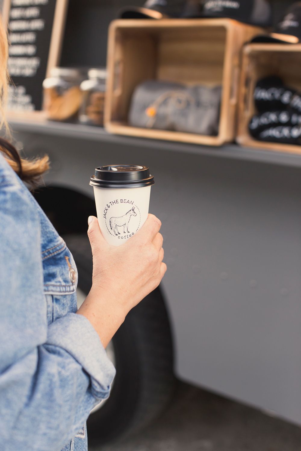 Hand holding white coffee cup with bear logo against wooden display shelves.