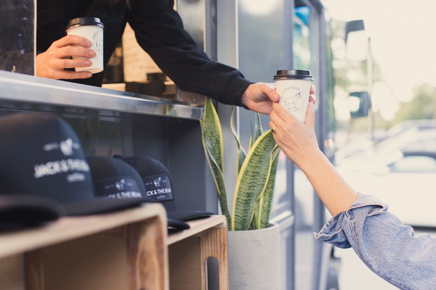 Hands exchanging Jack & The Bean coffee cups across retail merchandise display shelf.