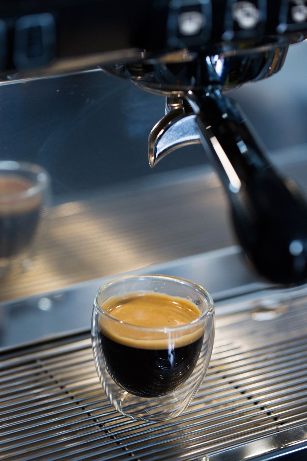 Double-walled glass cup of espresso with crema under an espresso machine spout.
