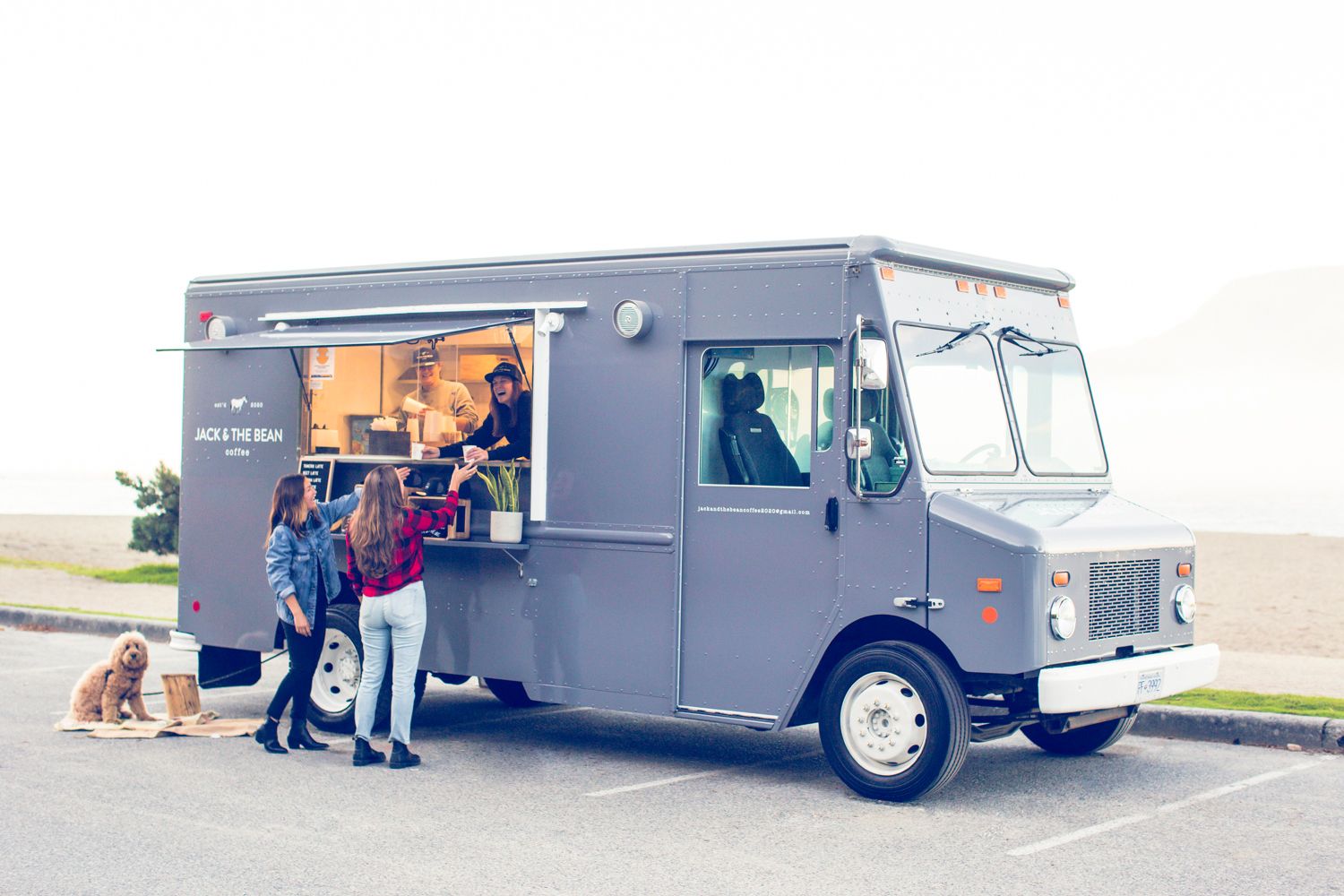 Grey food truck serving customers through service window on sunny day.